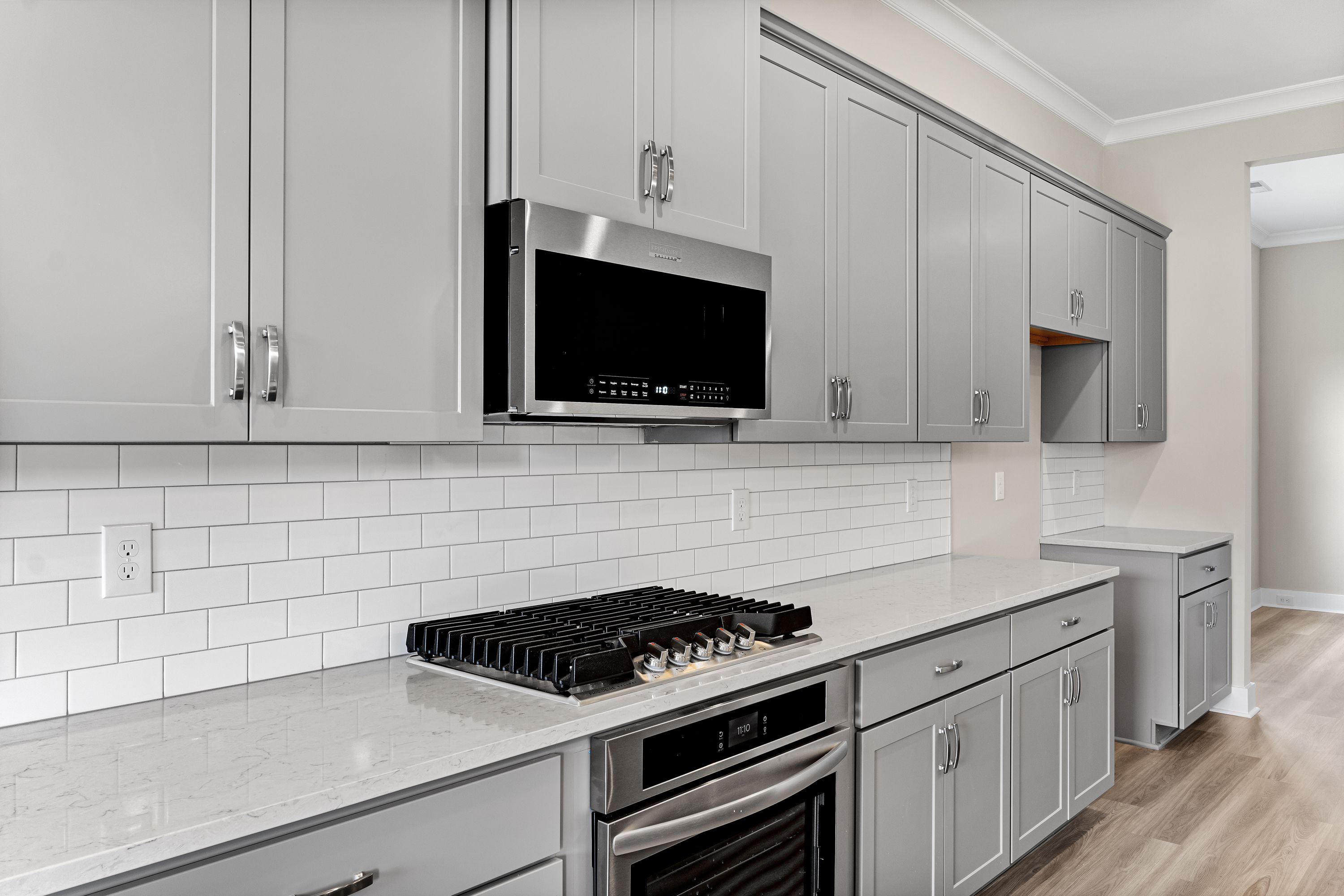 Modern kitchen in The Oxford A with gray shaker cabinets, white subway tile backsplash, quartz counters, and stainless steel appliances