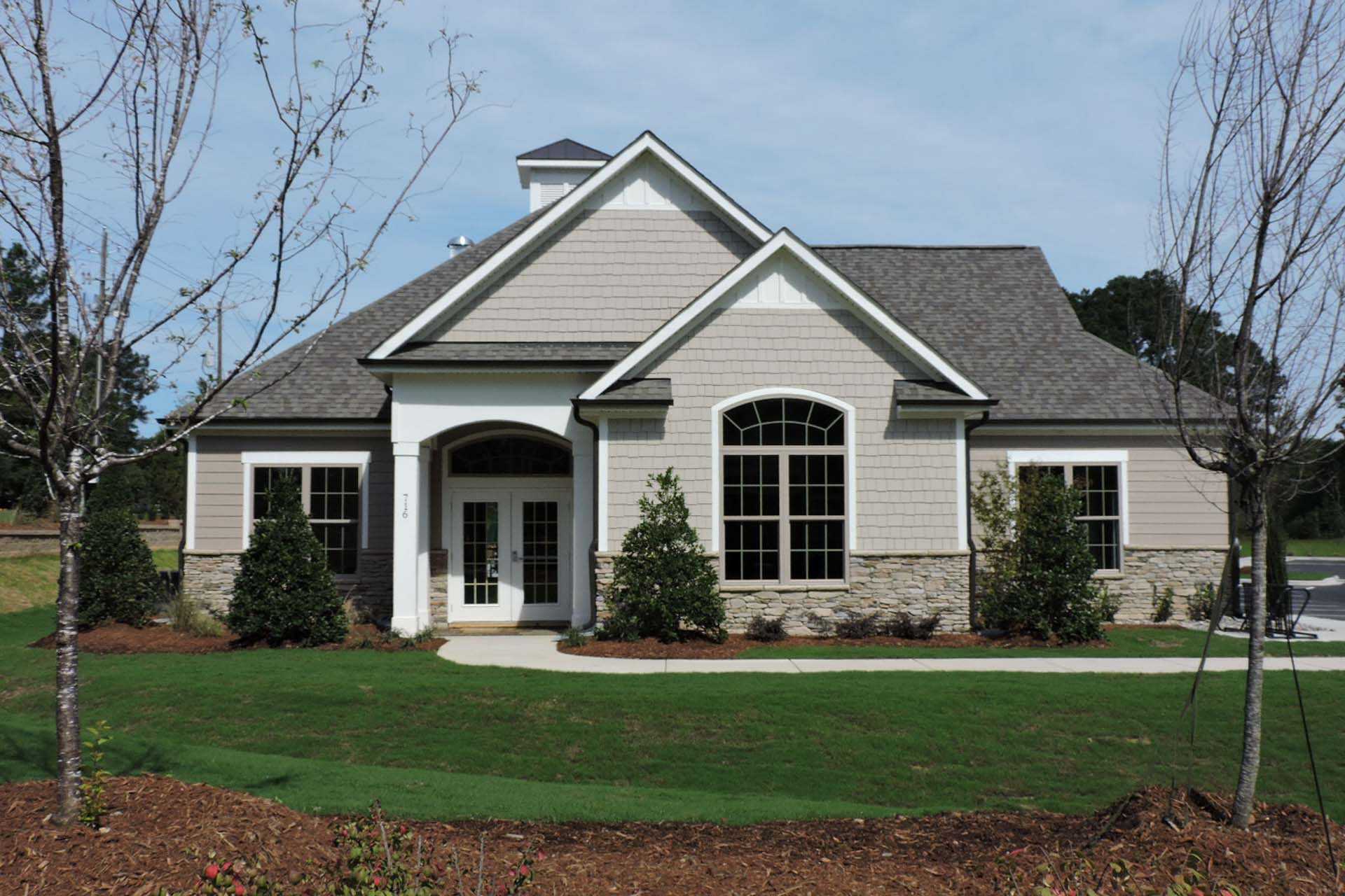 Modern clubhouse exterior at Glenmere in Knightdale NC with gabled roof arched windows covered porch and landscaped poolside grounds