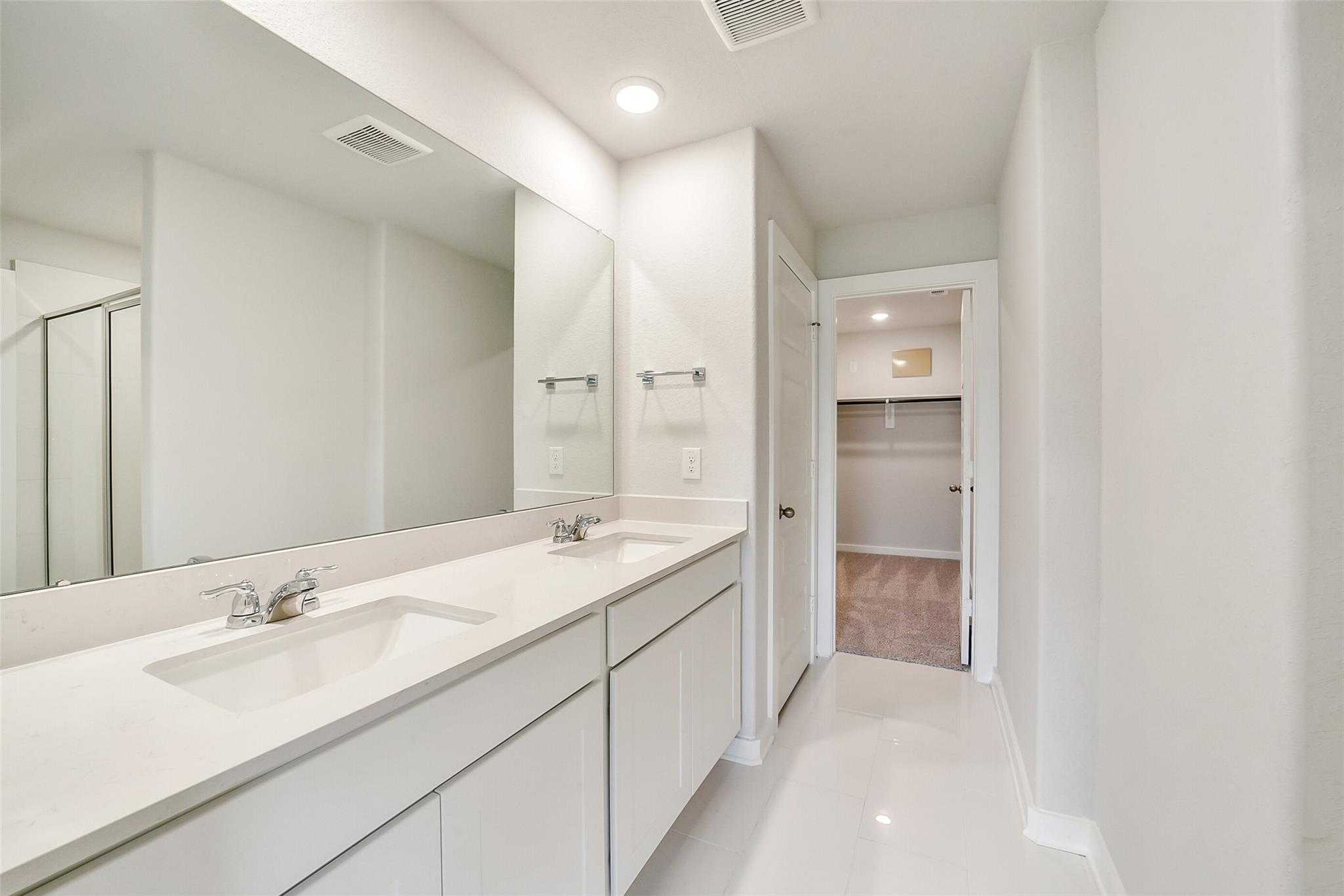 Modern master bathroom featuring double white vanity, large mirror, and walk-in closet in Davidson Homes The Trinity F, Magnolia, Texas