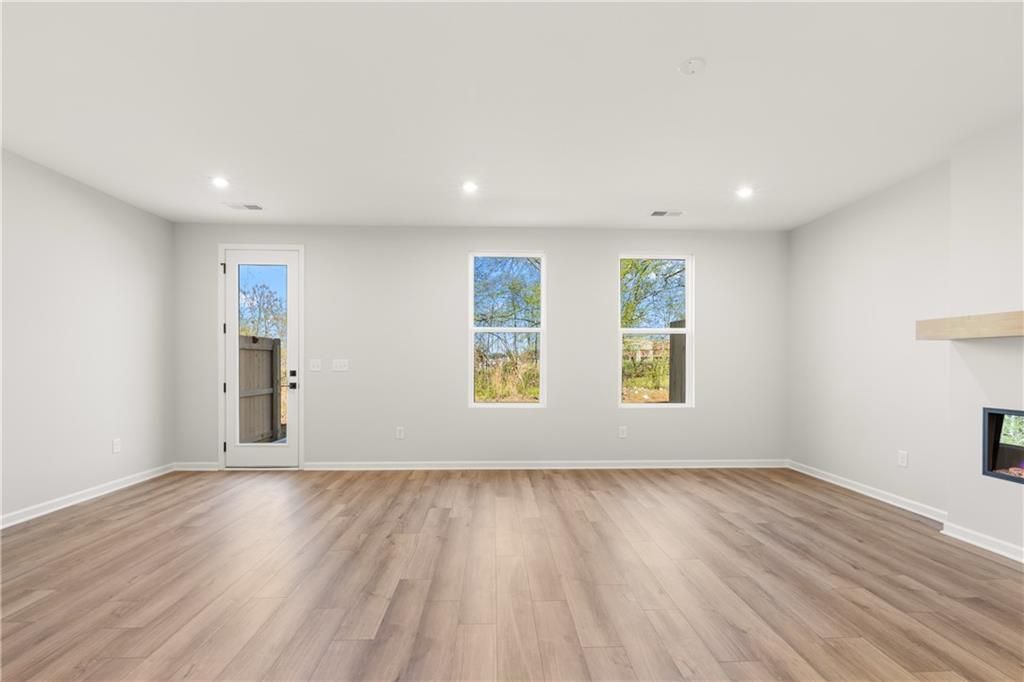 Spacious living room with hardwood floors, stone fireplace, large windows, and glass door in Davidson Homes The Cary A, Winder, Georgia