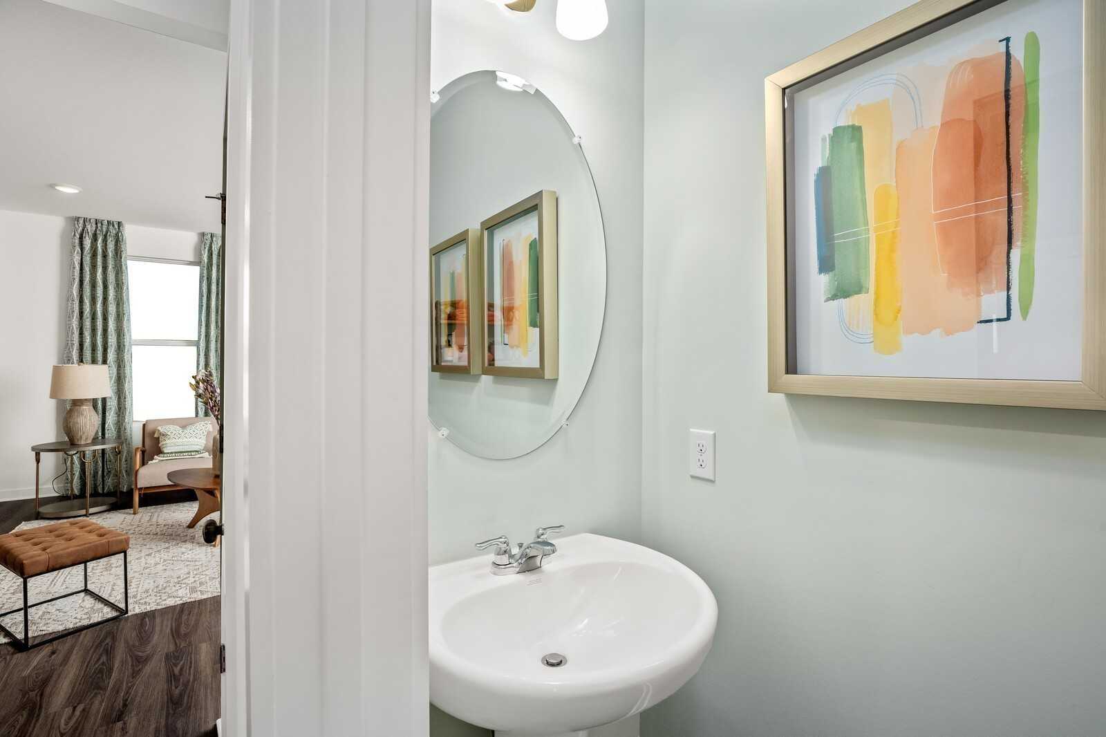 Elegant powder room with pedestal sink, round mirror, and abstract wall art in Davidson Homes The Gordon B, Sage Farms, White House, TN