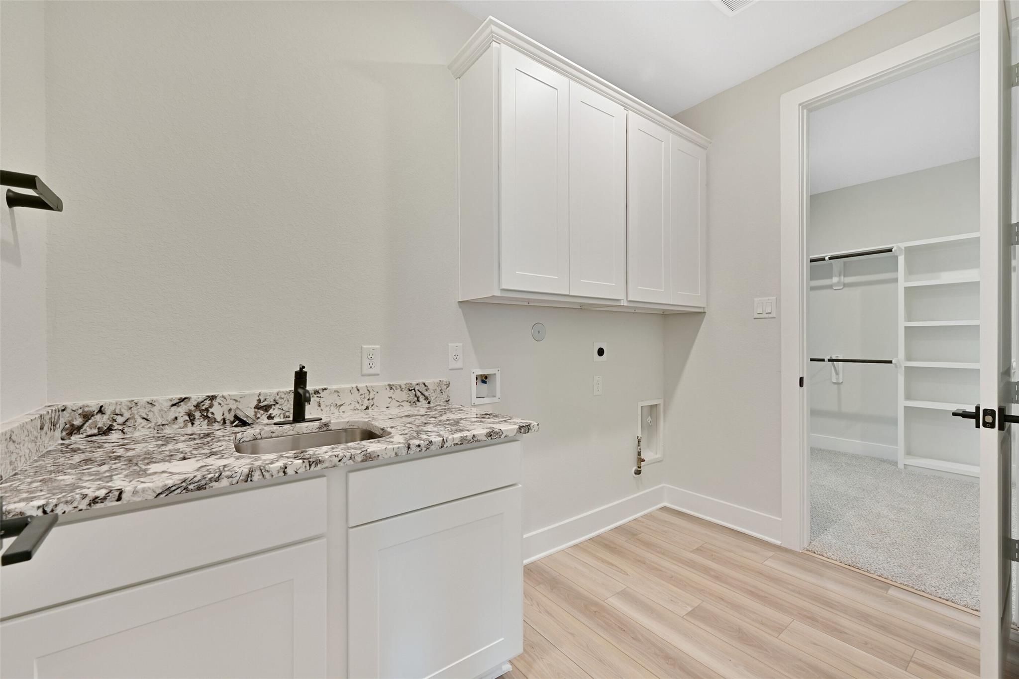 Modern laundry room with white cabinets, quartz counters, utility sink, and adjacent walk-in closet in Davidson Homes The Edward C, Lago Mar, Texas City