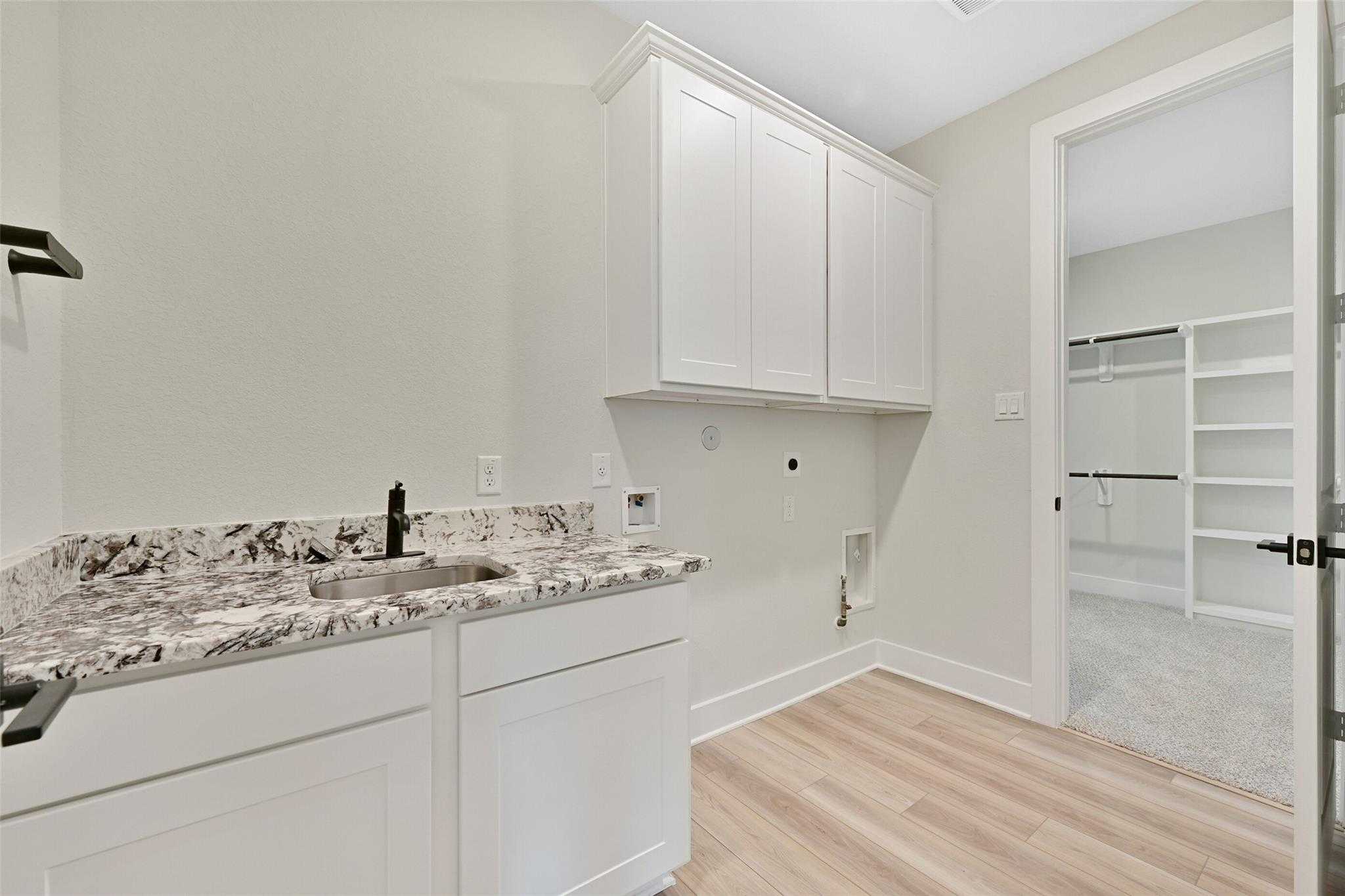 Modern laundry room with white shaker cabinets, quartz countertop utility sink, and adjacent walk-in closet in Davidson Homes Edward C, Texas City