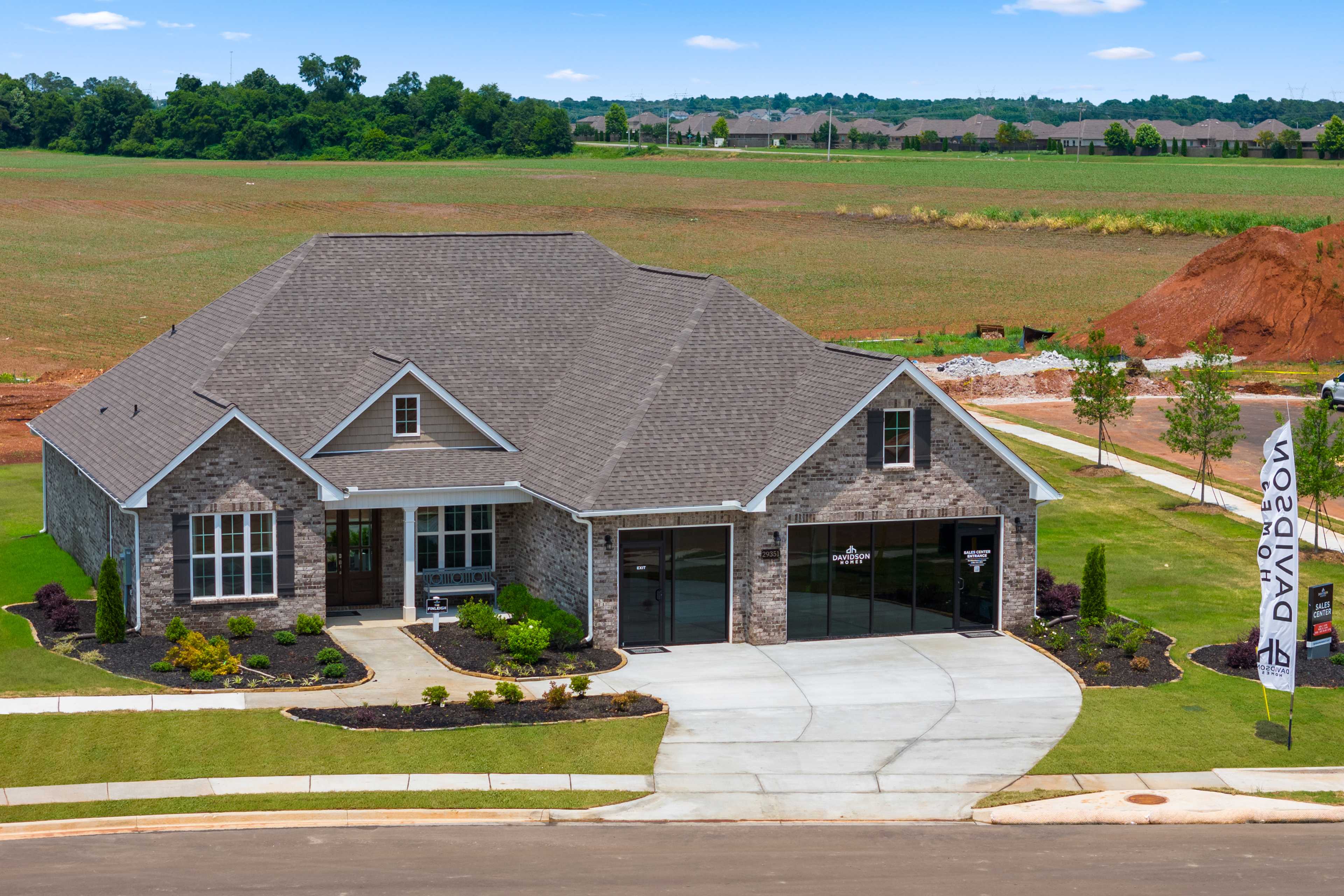 Modern ranch-style home exterior in Creekside, Harvest Alabama by Davidson Homes with stone facade, garage, and lush landscaping