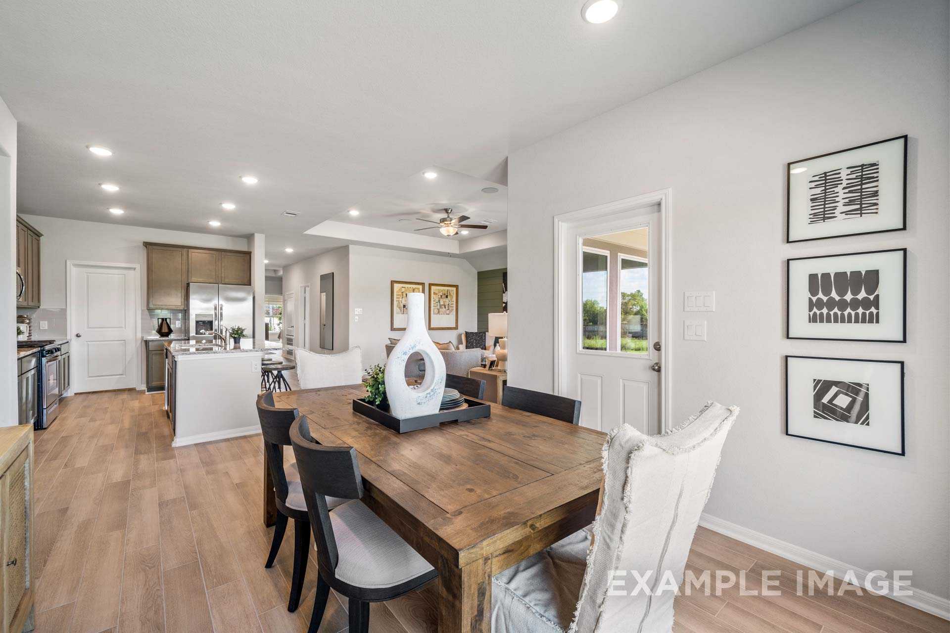 Open-concept kitchen dining in The Acadia B Davidson Homes plan, white cabinets island wooden table recessed lighting hardwood floors