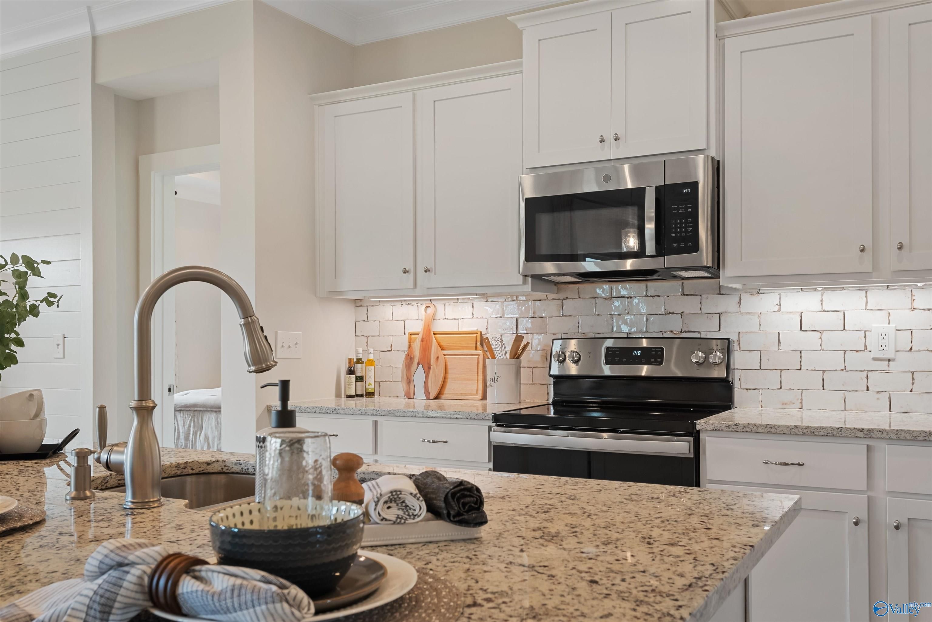 Modern kitchen featuring white shaker cabinets, beige granite counters, stainless steel appliances in Davidson Homes The Everett, New Market, Alabama