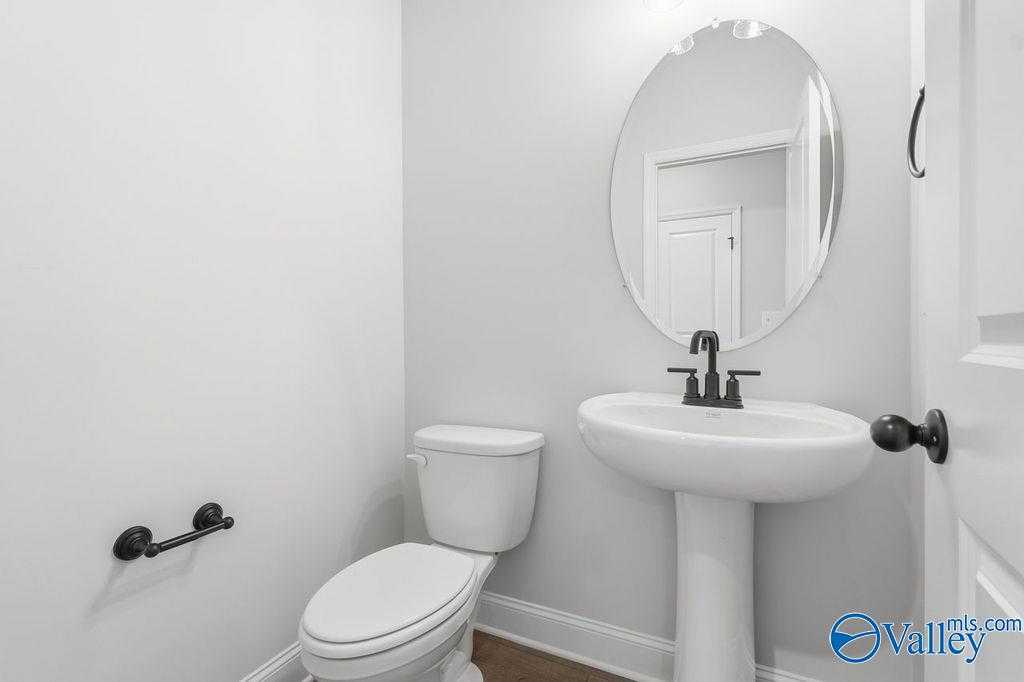 Elegant powder room with pedestal sink, round mirror, black fixtures, and white toilet in Davidson Homes The Rockford B, Hartselle, Alabama