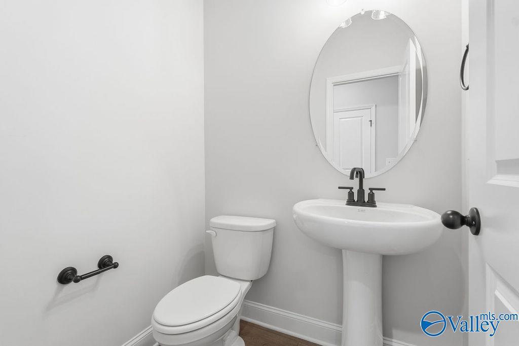 Elegant powder room with white pedestal sink, round mirror, and toilet in Davidson Homes The Rockford B, Hartselle, Alabama