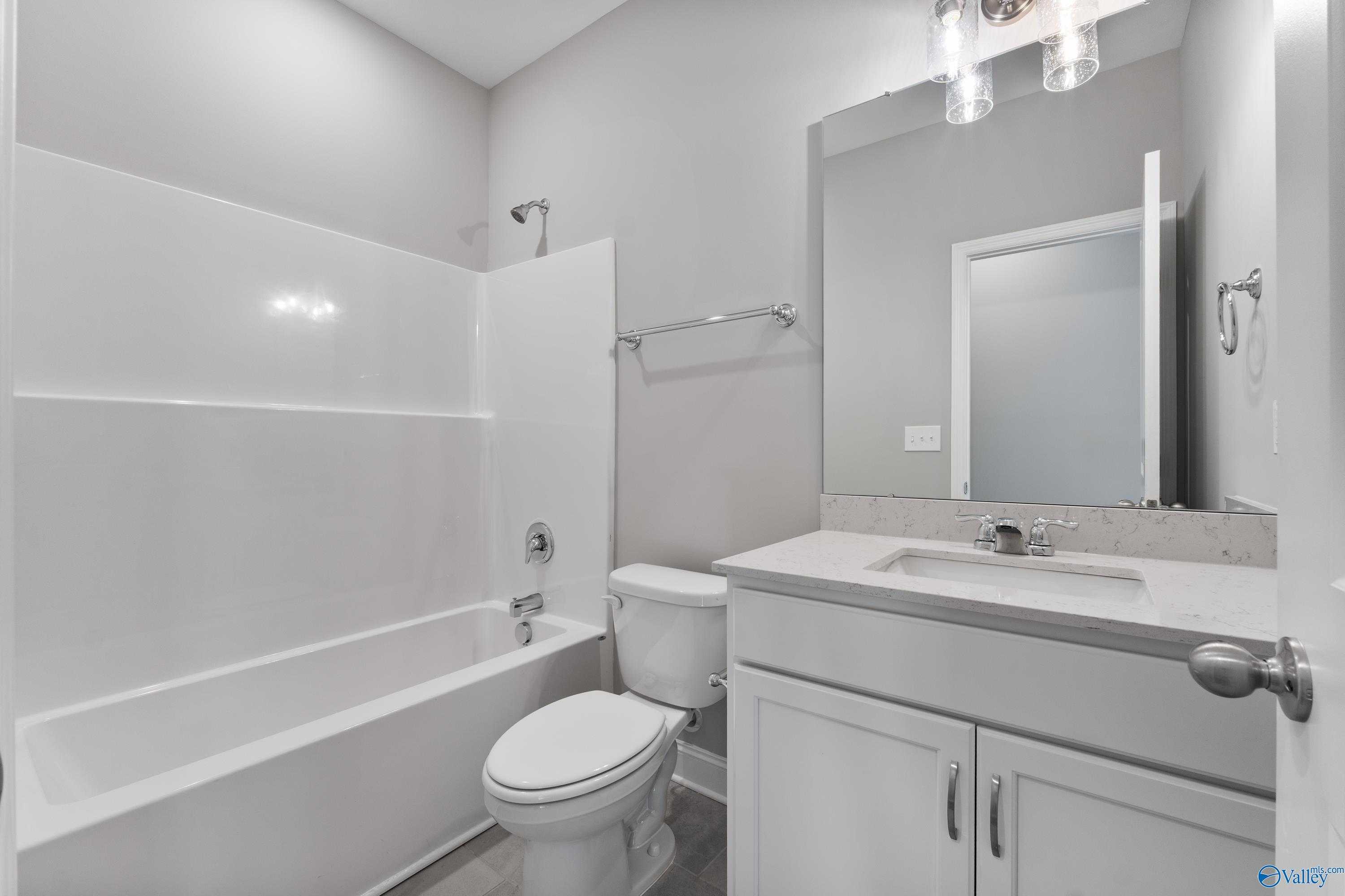 Modern bathroom with white tiled tub-shower combo, vanity, and toilet in Davidson Homes The Rockford, Harvest, Alabama