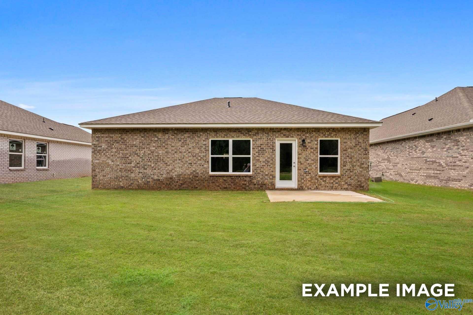 Back view of Davidson Homes The Butler 3-bed brick house with glass door, windows, concrete patio, and green yard in Wood Trail, Toney, AL