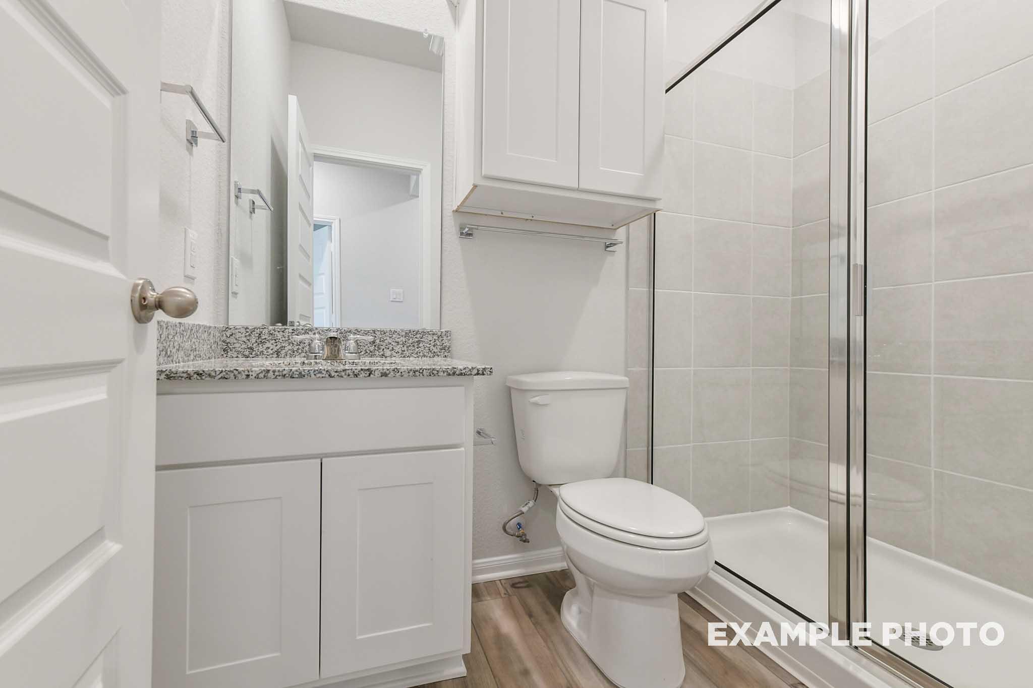 Modern bathroom in The Frio floor plan featuring a granite vanity, white cabinetry, and a glass-enclosed walk-in shower.