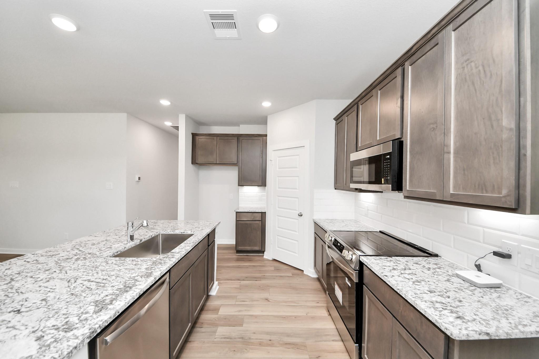 Modern kitchen with granite countertops, stainless appliances, and subway tile in The Sabine E floor plan, Cleveland, TX.