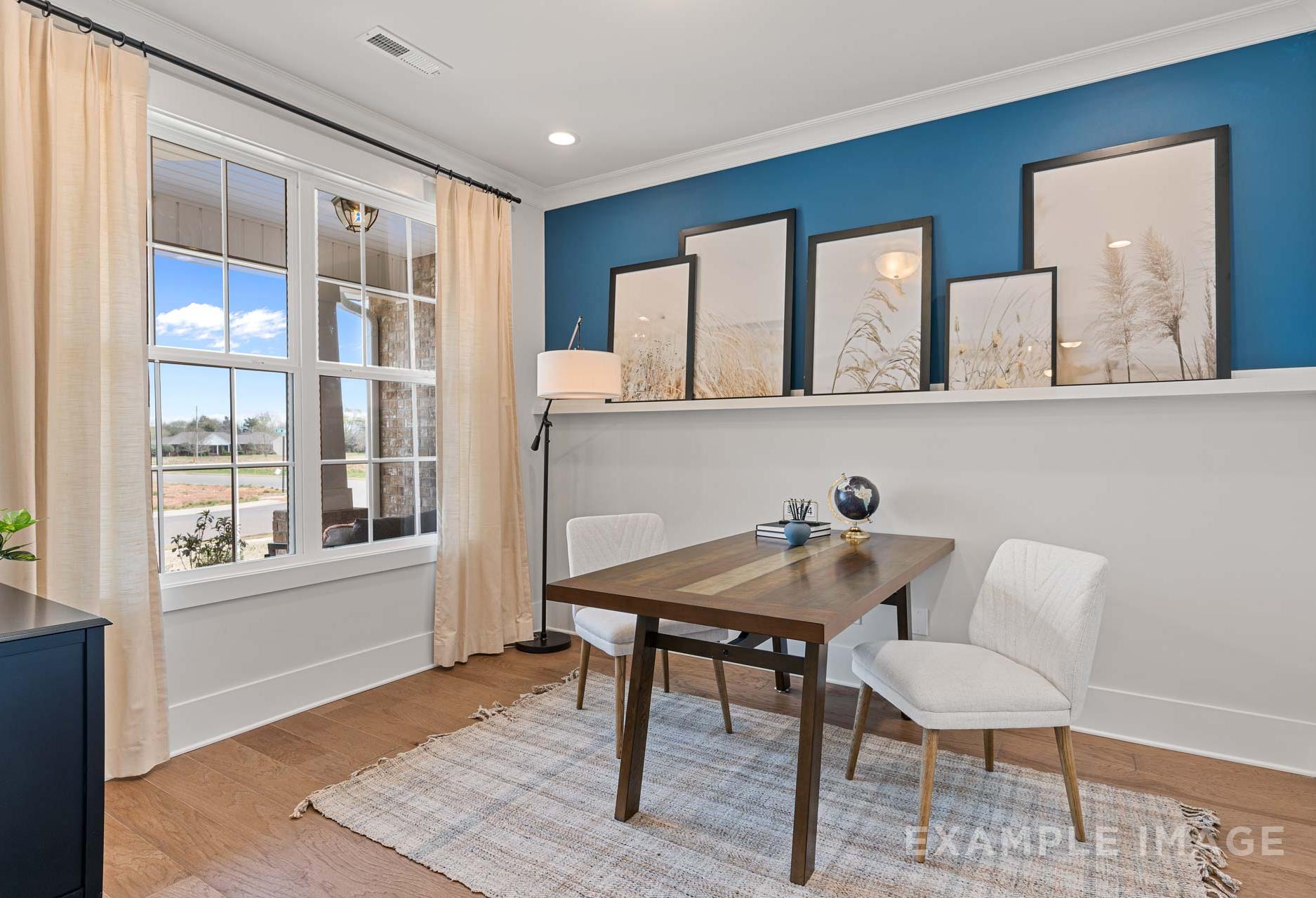 Spacious home office in The Rockford with blue accent wall, wooden desk, white chairs, and large windows overlooking fields