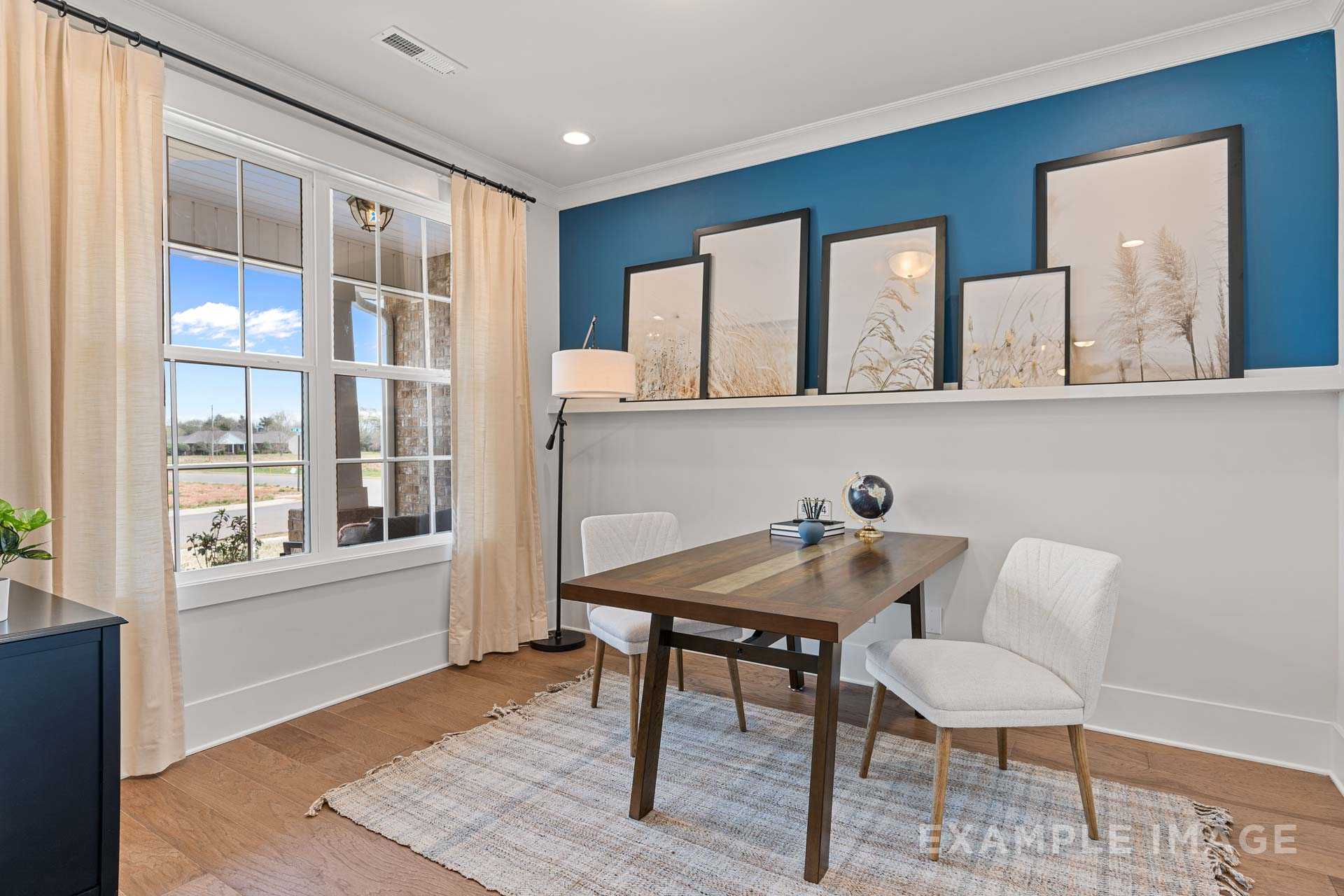 Spacious home office in The Rockford with blue accent wall, wooden desk, white chairs, and large windows overlooking fields