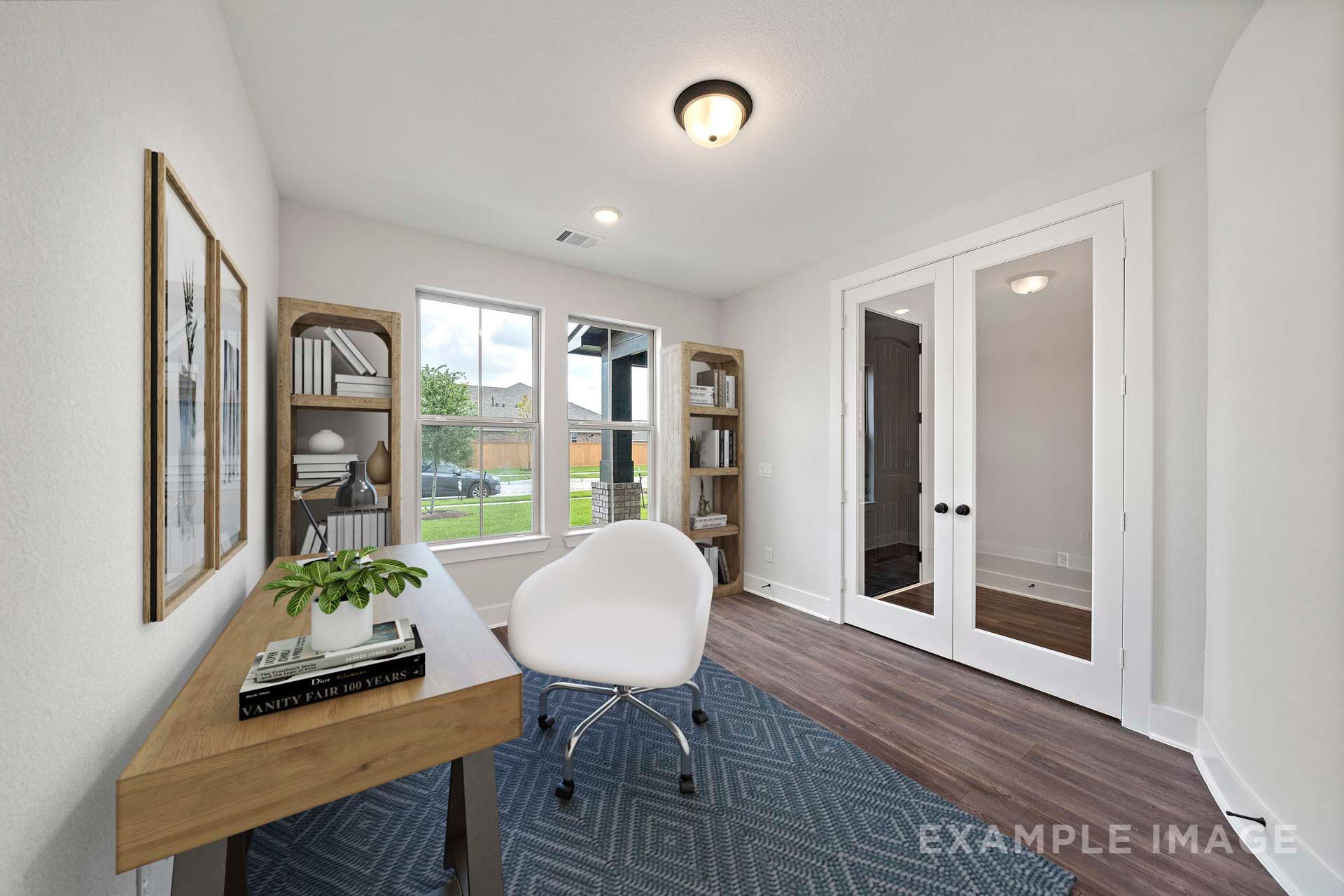 Bright home office in The Victoria by Davidson Homes featuring French doors, wood desk, white chair, and natural light.