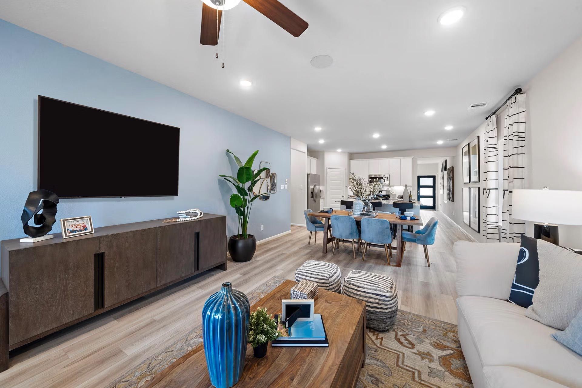 Open-concept living dining room at Saddle Creek Ranch in Cibolo Texas with blue accent wall, mounted TV, hardwood floors, ceiling fan, and modern furniture