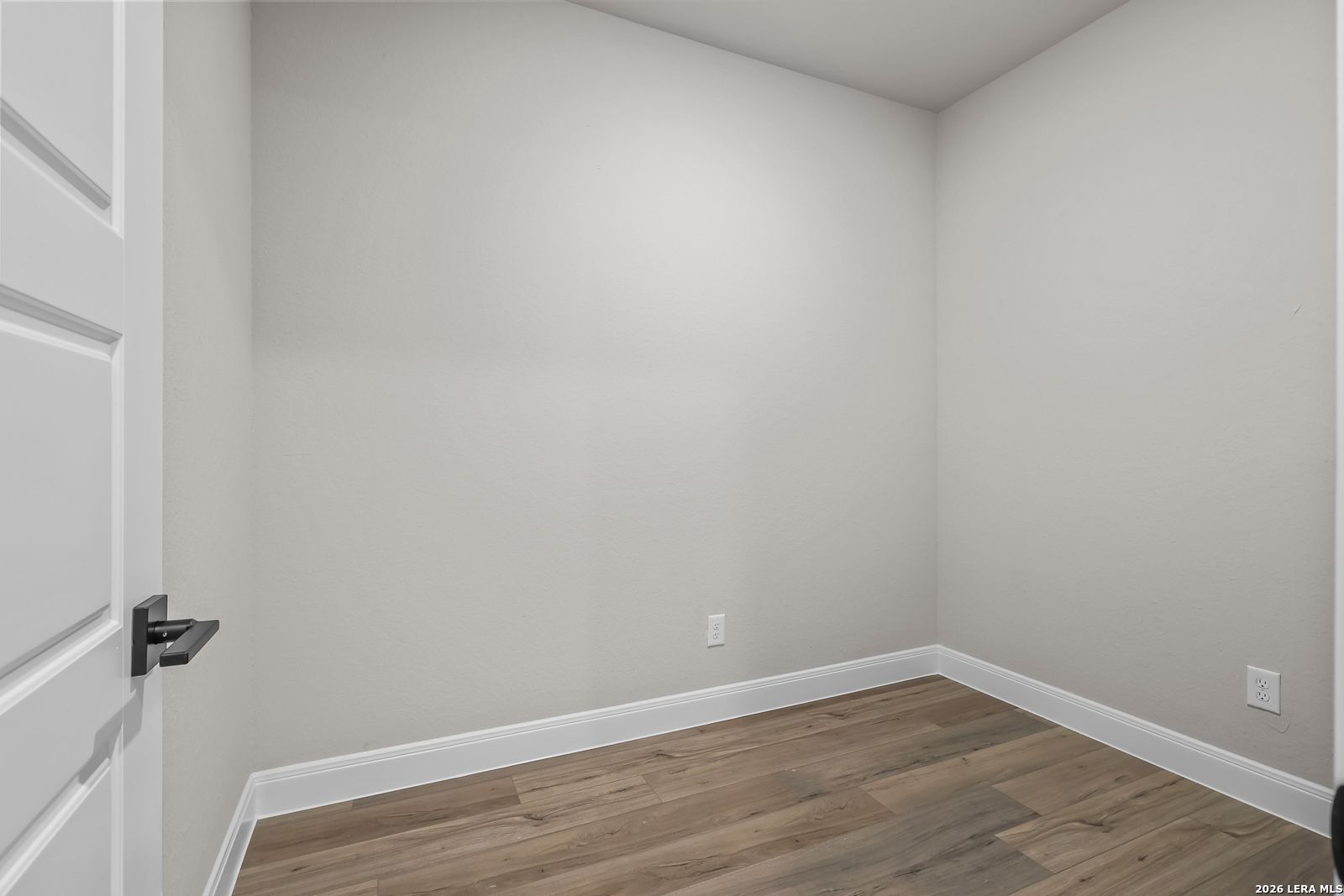 Empty bedroom with neutral walls, wood-look flooring, and modern black door hardware in Davidson Homes The Foster E, Castroville, Texas