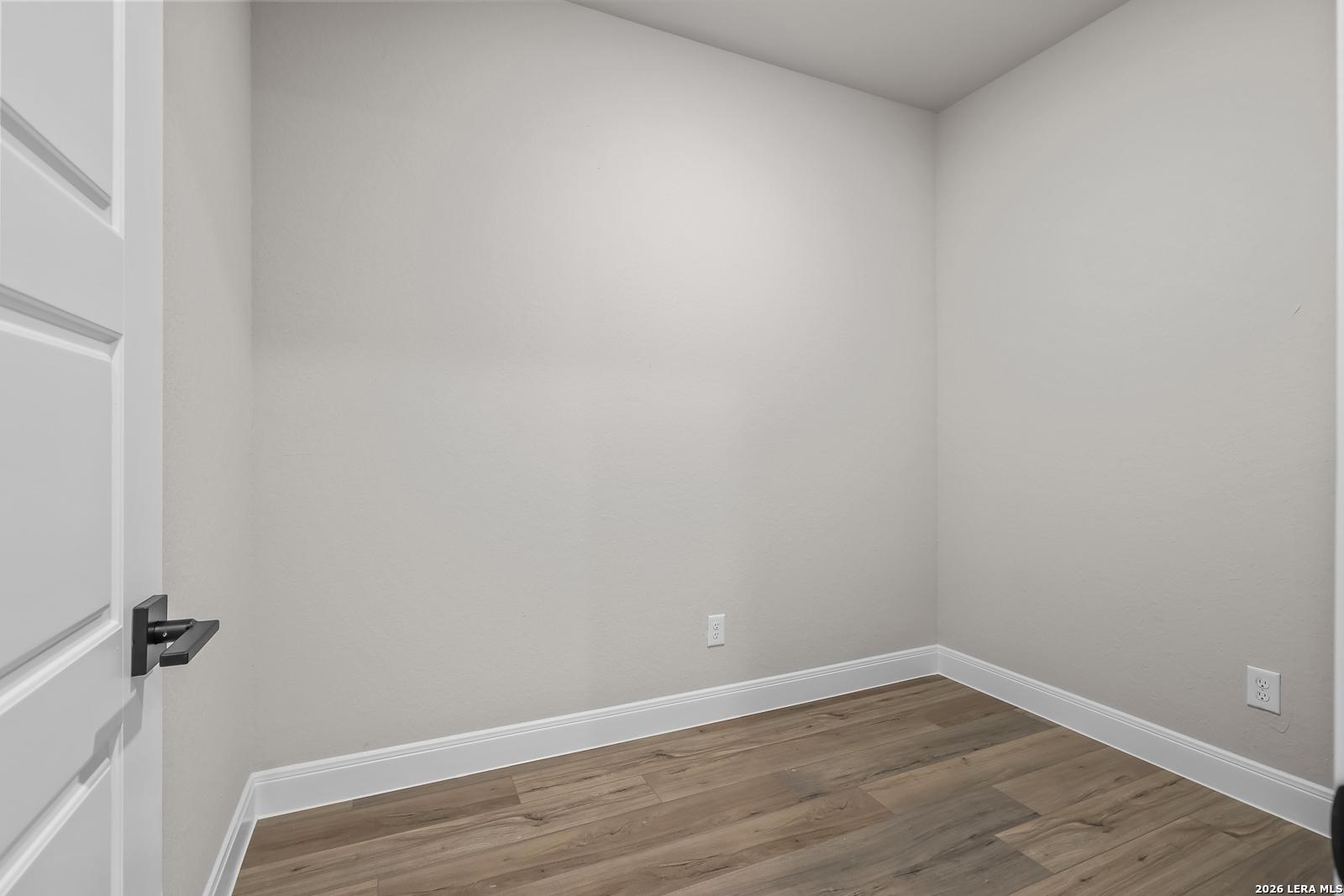 Empty bedroom with neutral walls, wood-look flooring, and modern black door hardware in Davidson Homes The Foster E, Castroville, Texas