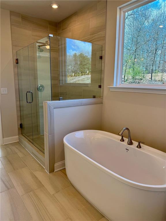 Luxurious master bathroom with freestanding white tub, frameless glass shower, tiled walls, and window view in Davidson Homes The Danbury C, Buford, GA