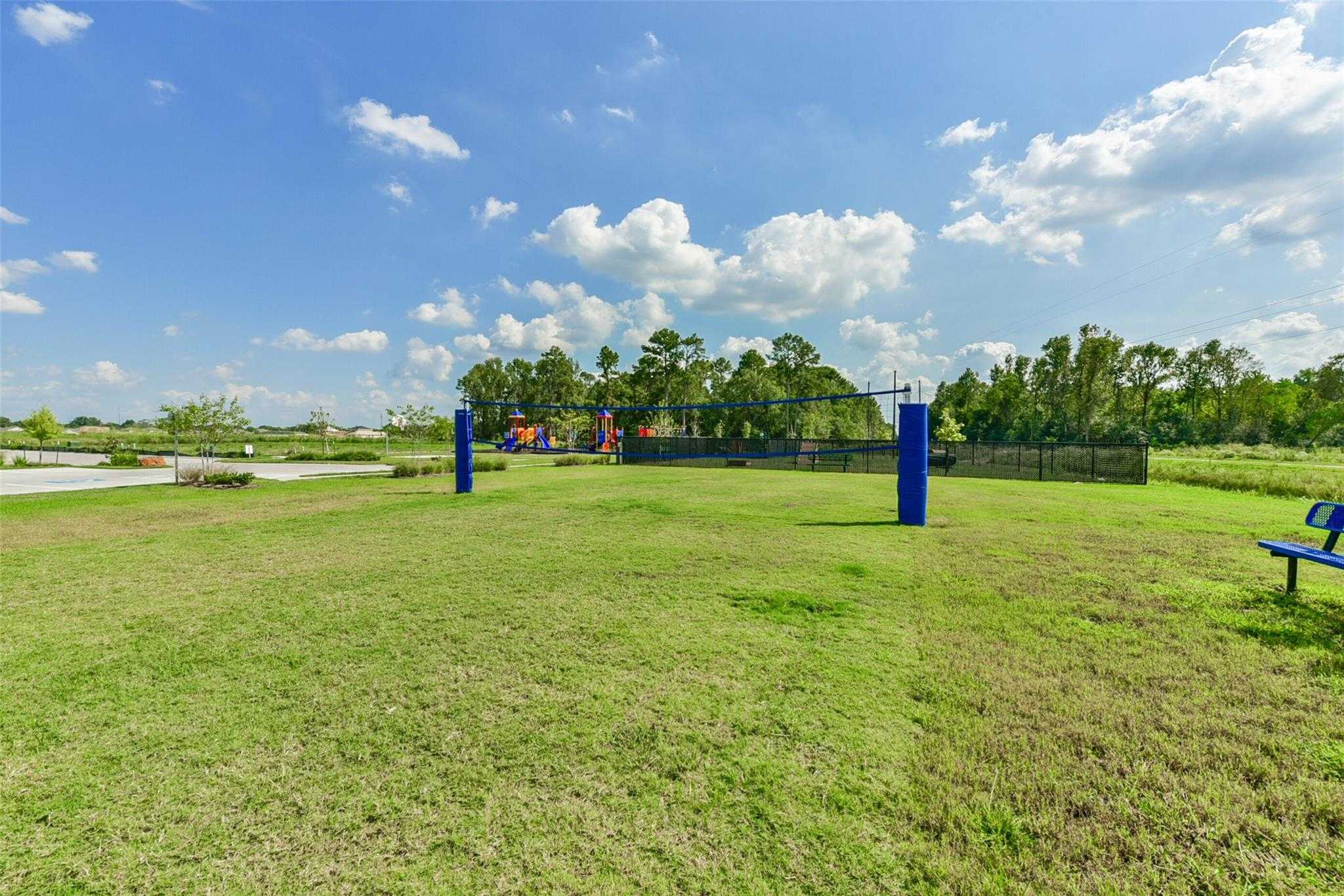 Community volleyball court in grassy park with playground, trees, and benches in The Villages at WestPointe, Dayton, Texas