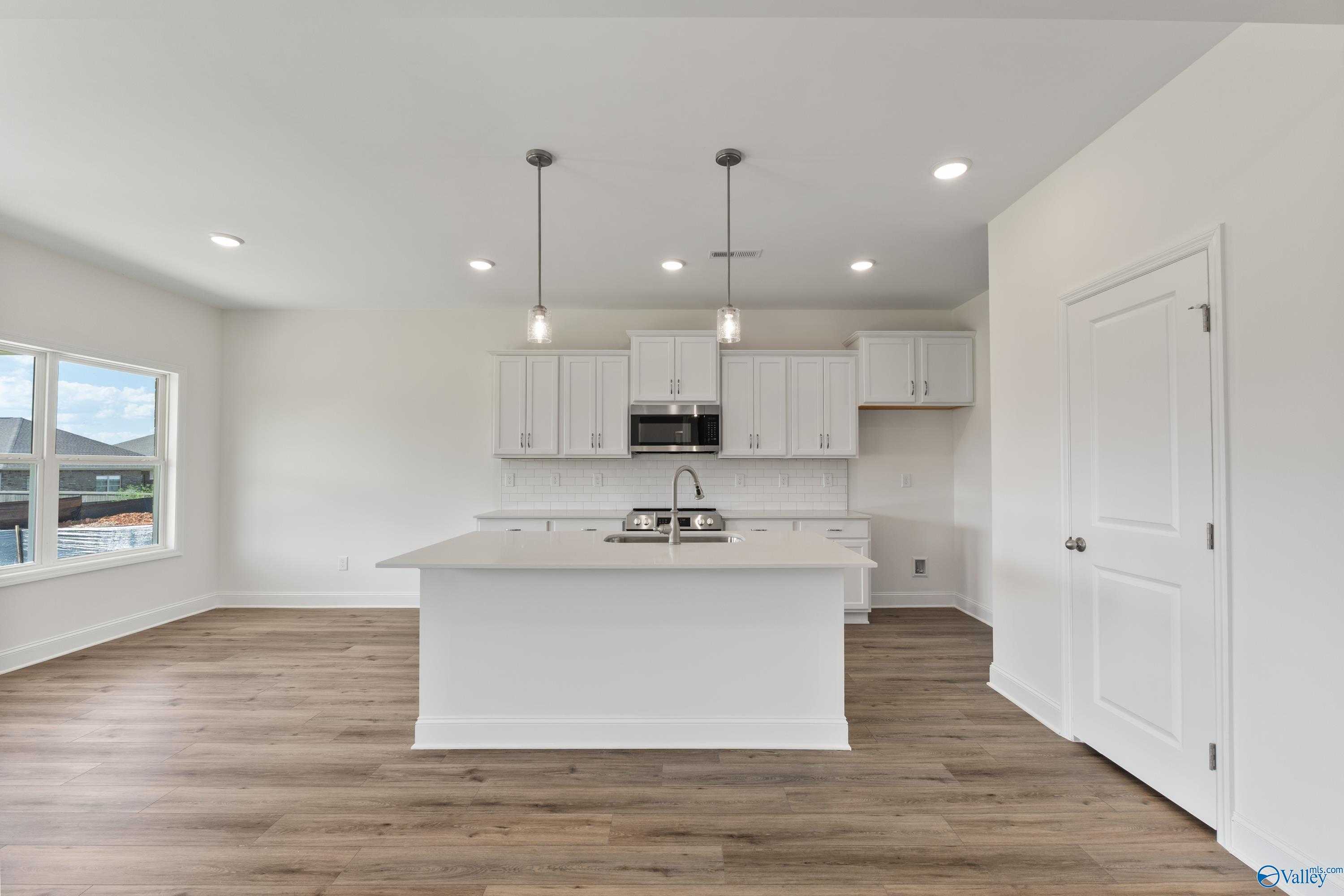Bright modern kitchen with white shaker cabinets, large island sink, stainless microwave, pendant lights, and hardwood floors in The Shelby A home, New Market, AL