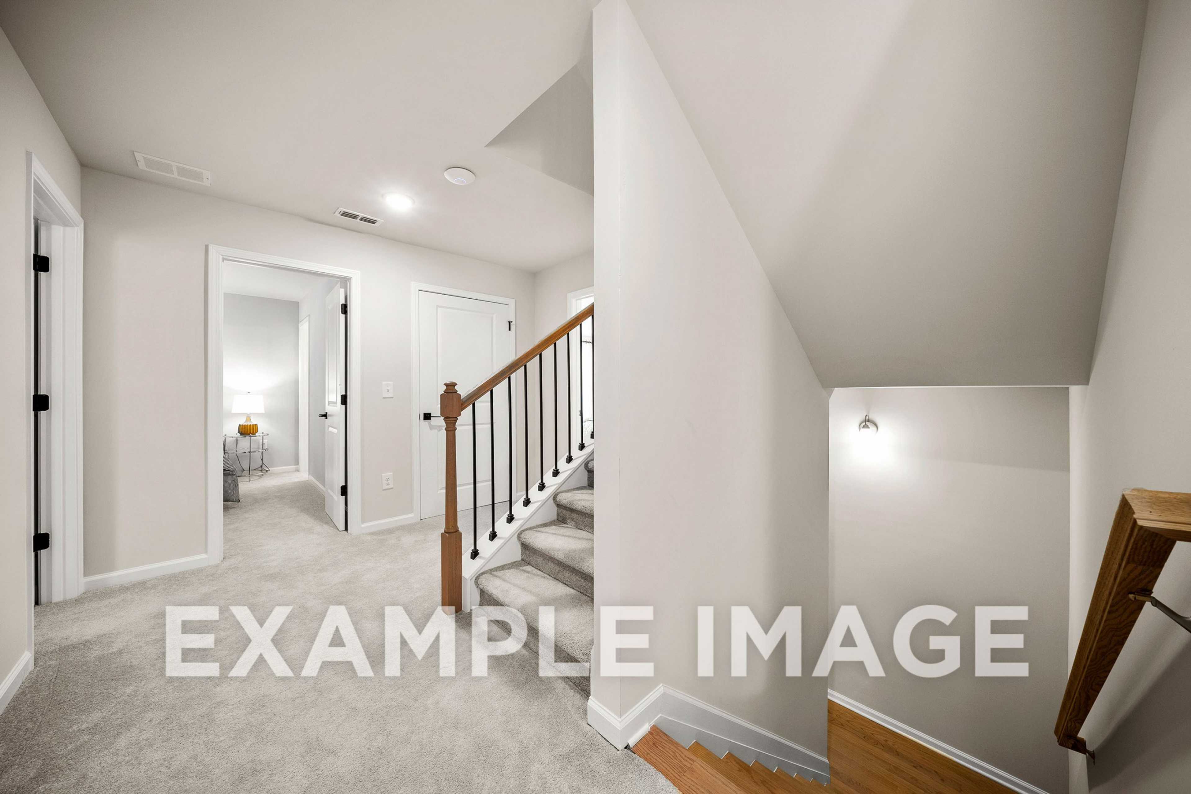 Spacious upstairs hallway in The Hickory A showcasing wooden staircase, bedroom doors, and neutral carpeted floors in Davidson Homes design
