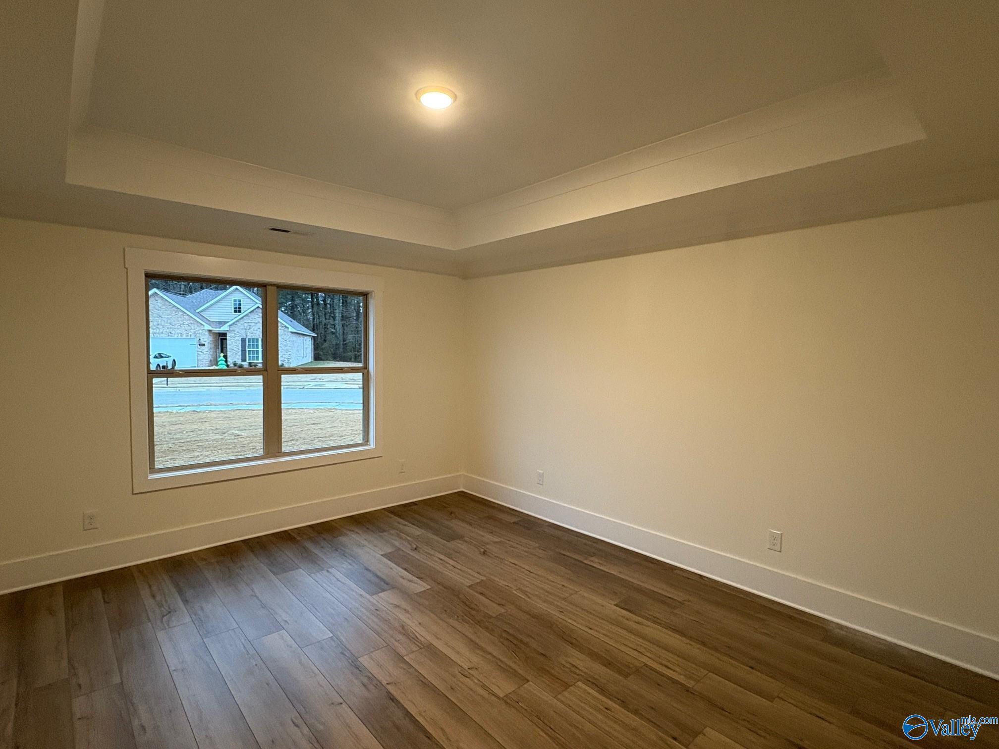 Bright bedroom featuring tray ceiling, large windows with wooded view, and light wood floors in Davidson Homes The Daphne C, Arab, Alabama