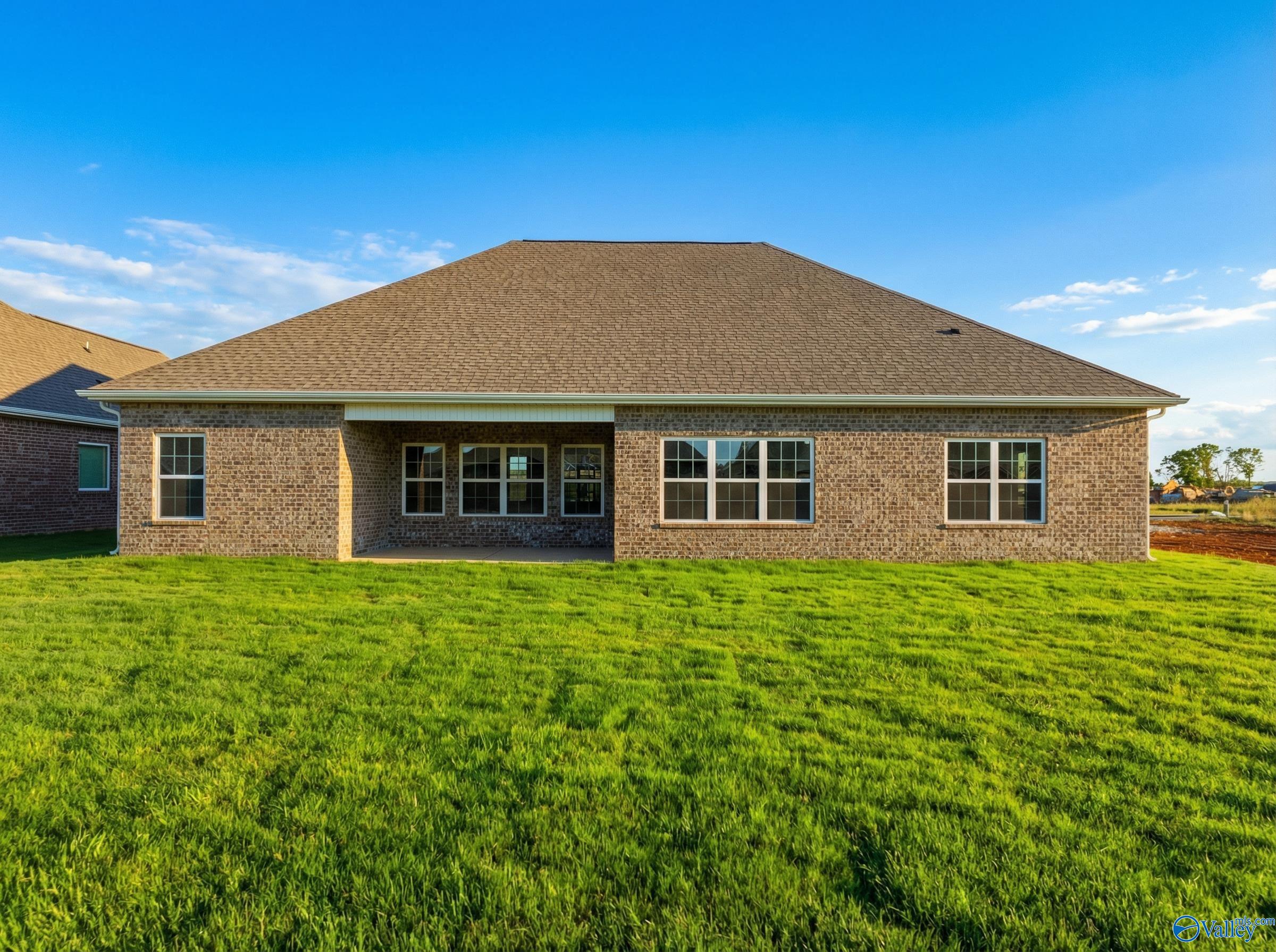 Back view of The Finleigh single-story brick home with covered patio, large windows, and lush green yard in Briercreek, Meridianville, Alabama