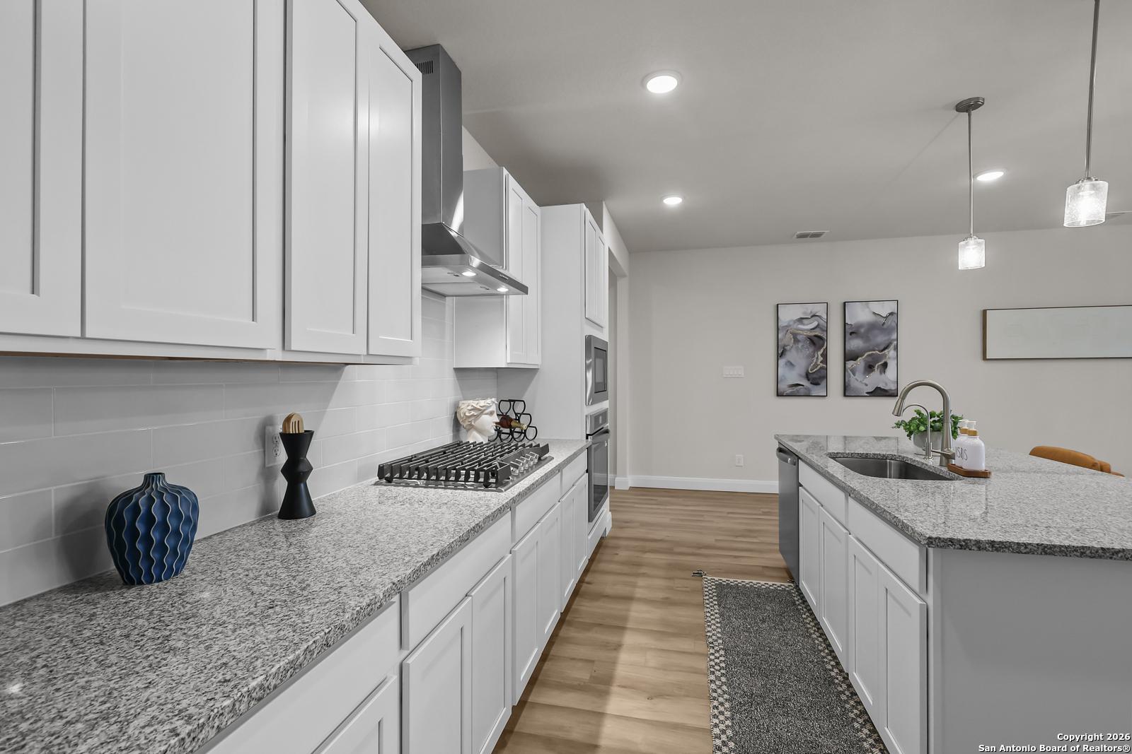 Modern white kitchen with granite countertops, stainless steel range, and island sink in The Lanier H floor plan, Ladera San Antonio