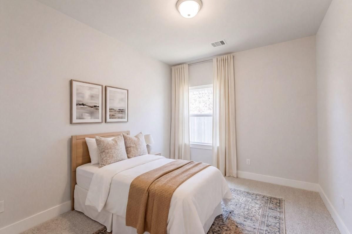 Cozy secondary bedroom with queen bed, neutral bedding, abstract art, and sheer curtains in Davidson Homes The Luna J, Sunterra, Katy
