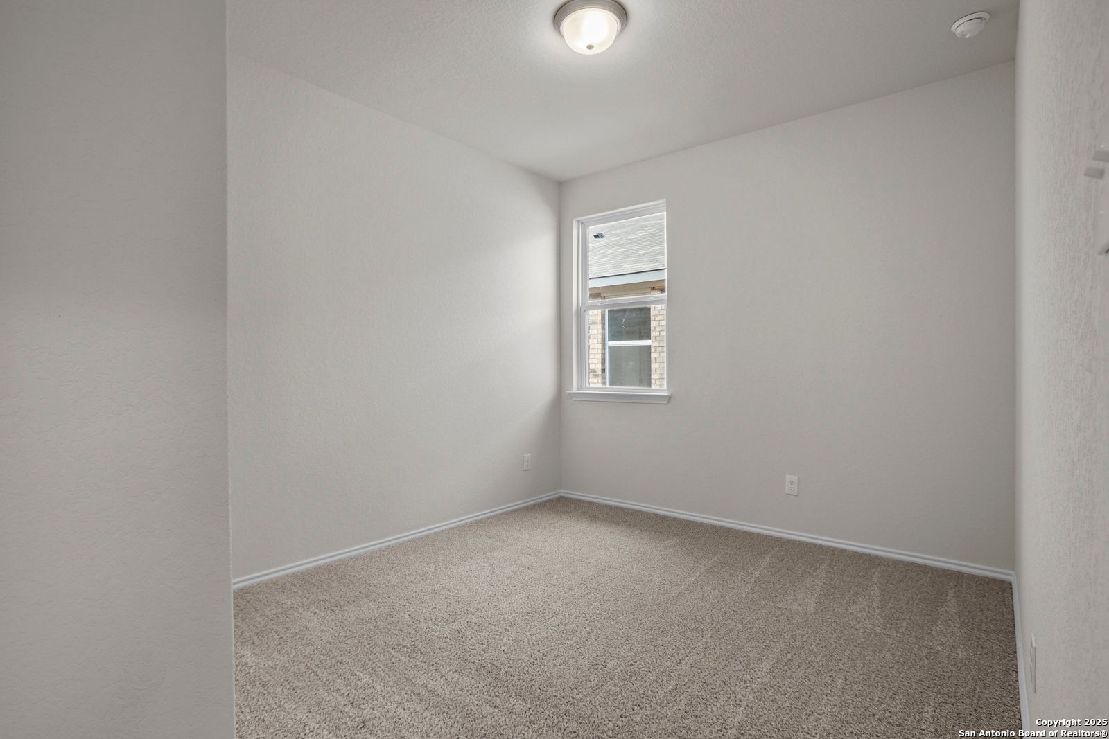 Empty bedroom with neutral beige walls, tan carpet flooring, window AC unit, and flush ceiling light in Davidson Homes The Asheville J, San Antonio, TX