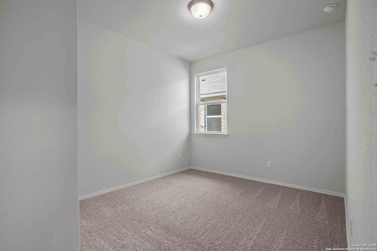 Empty bedroom with neutral beige walls, tan carpet flooring, window AC unit, and flush ceiling light in Davidson Homes The Asheville J, San Antonio, TX