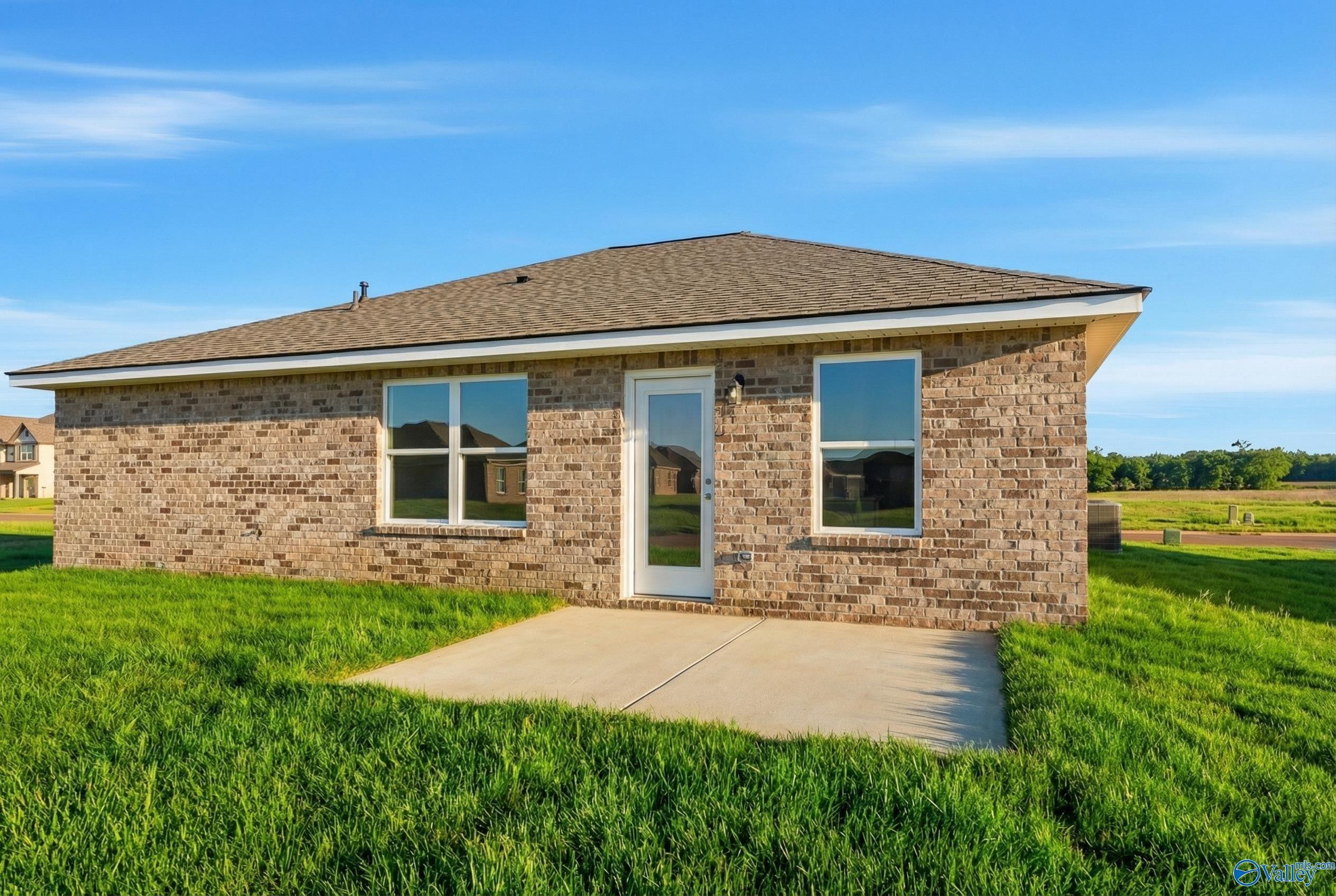 Single-story brick home with gabled roof, large windows, front door, and concrete patio in green yard, Heritage Lakes, New Market, Alabama