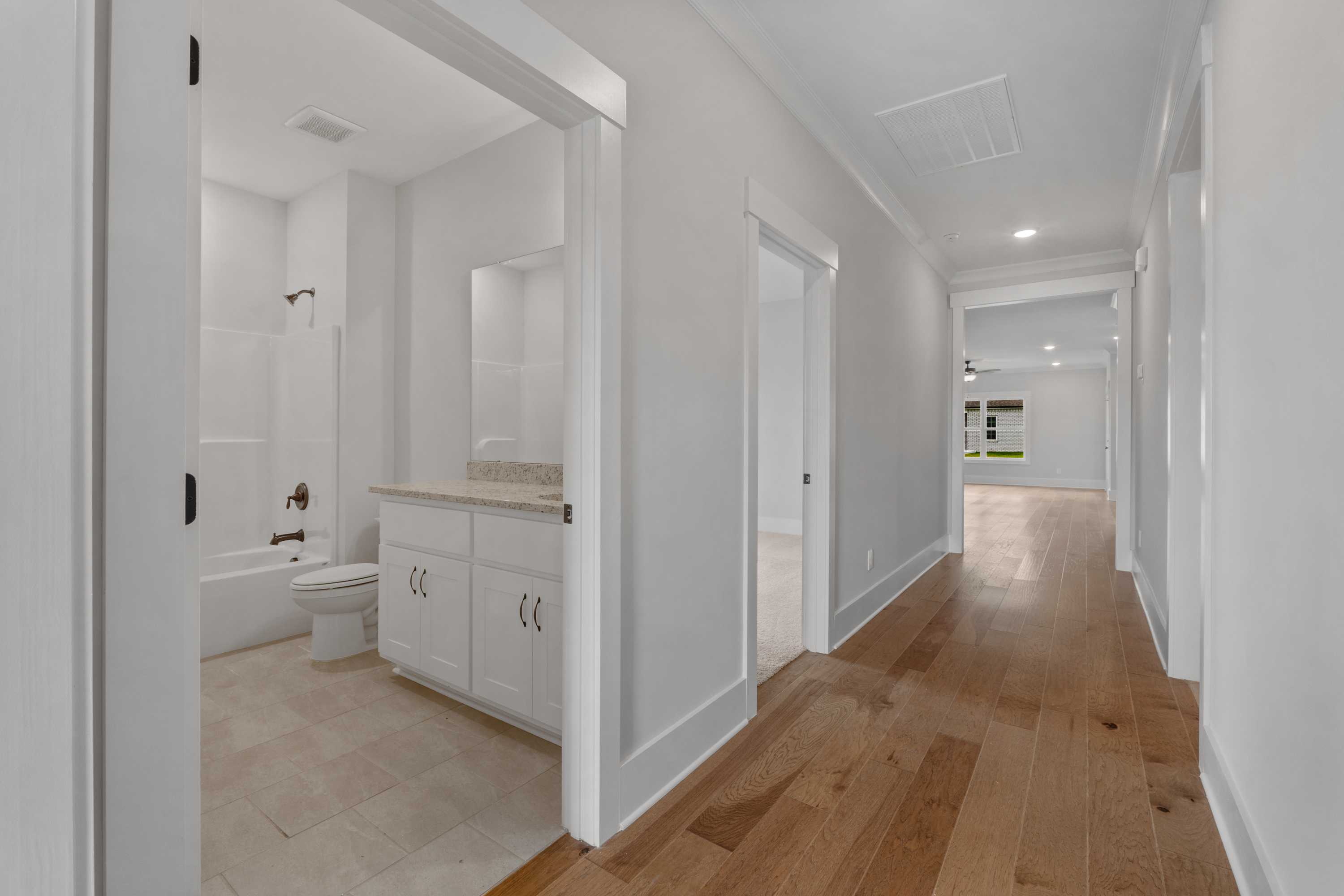 White tiled bathroom with bathtub, vanity and shower next to hardwood hallway at The Villas at Barnett's Crossing, Madison AL