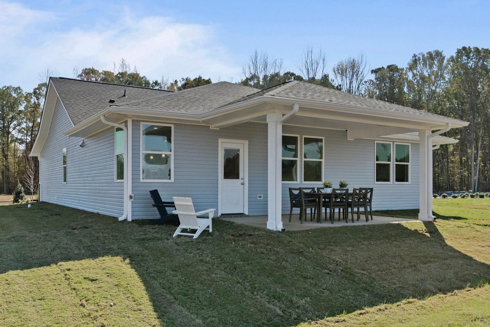 Rear view of Phoenix A single-story home featuring covered porch, outdoor dining area, and lush green yard in Opelika