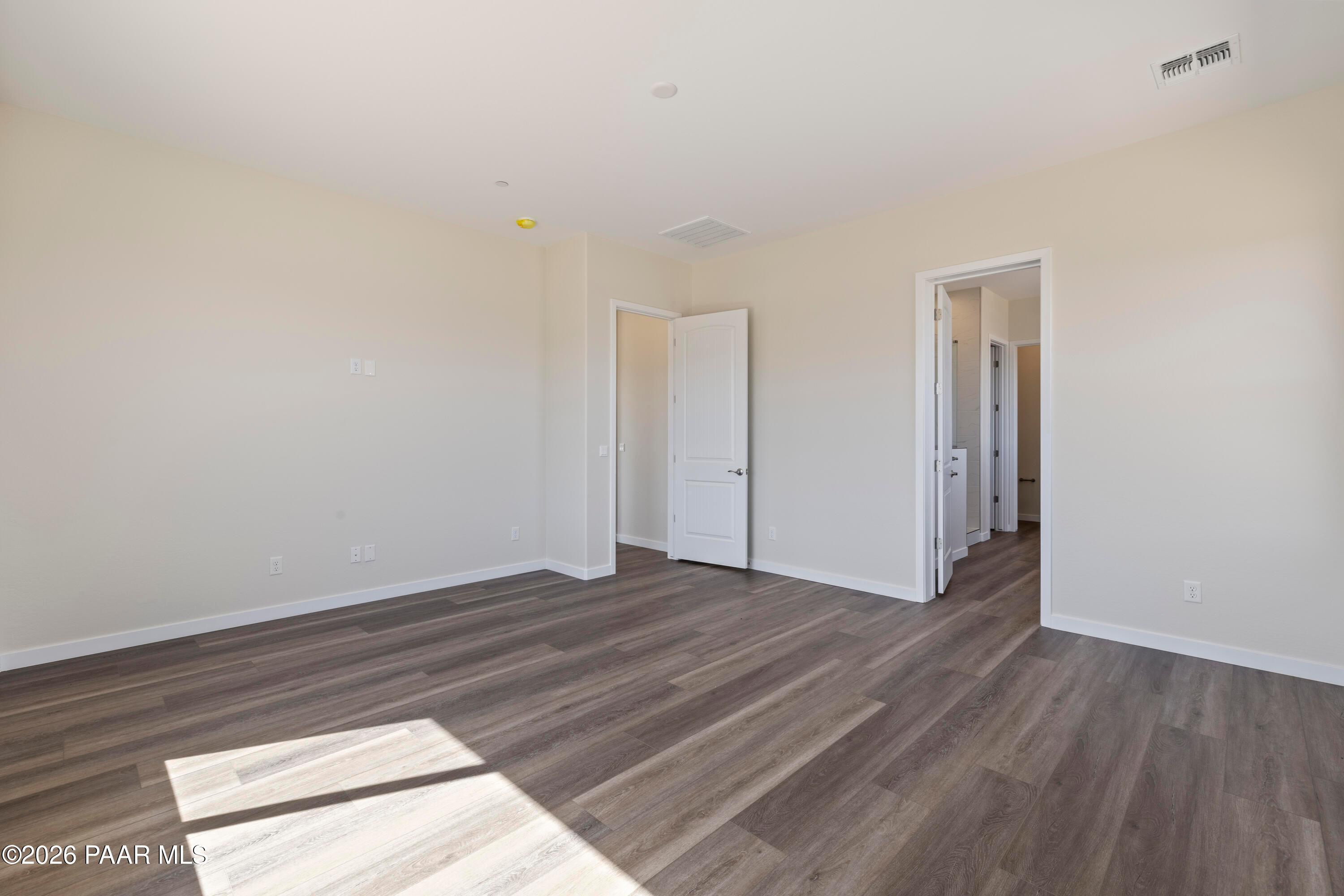 Spacious empty bedroom with beige walls, wood-look flooring, and open doorways in Davidson Homes Soleil E, Prescott Arizona