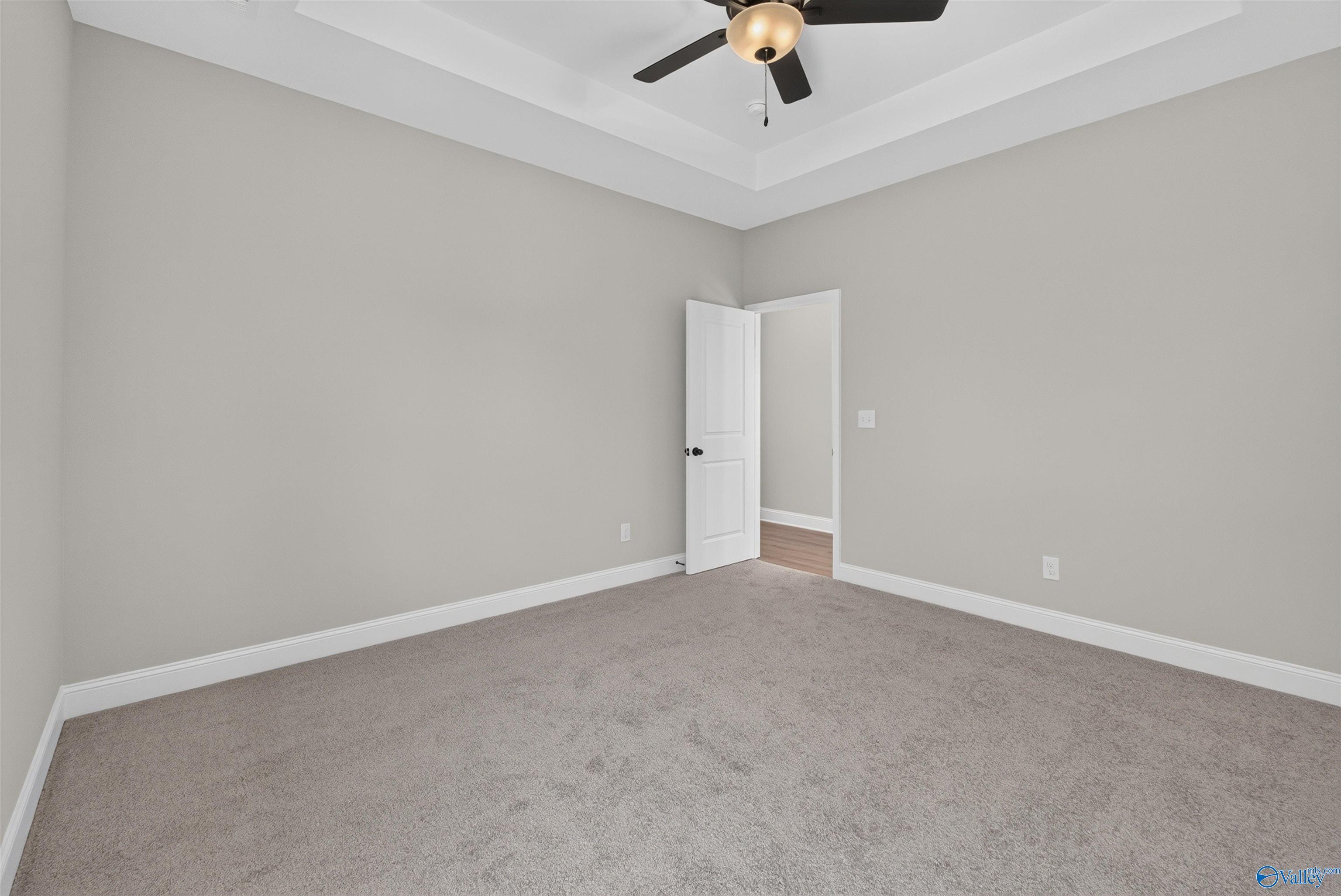 Spacious carpeted bedroom with tray ceiling and ceiling fan in Davidson Homes The Butler floor plan, Hazel Green, Alabama