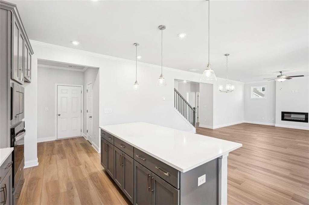 Open-concept kitchen with gray shaker cabinets, white quartz island, stainless appliances, adjacent to living room featuring gas fireplace and hardwood floors in Davidson Homes The Hickory C, Hoschton, GA