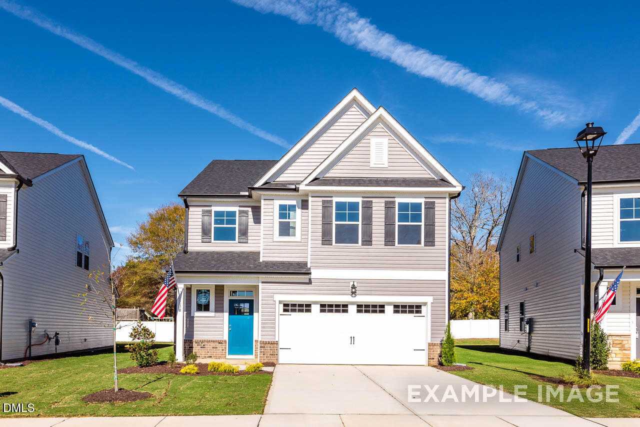 Modern two-story gray home with blue door, two-car garage, American flags, and landscaped yard in Gregory Village, Lillington, NC