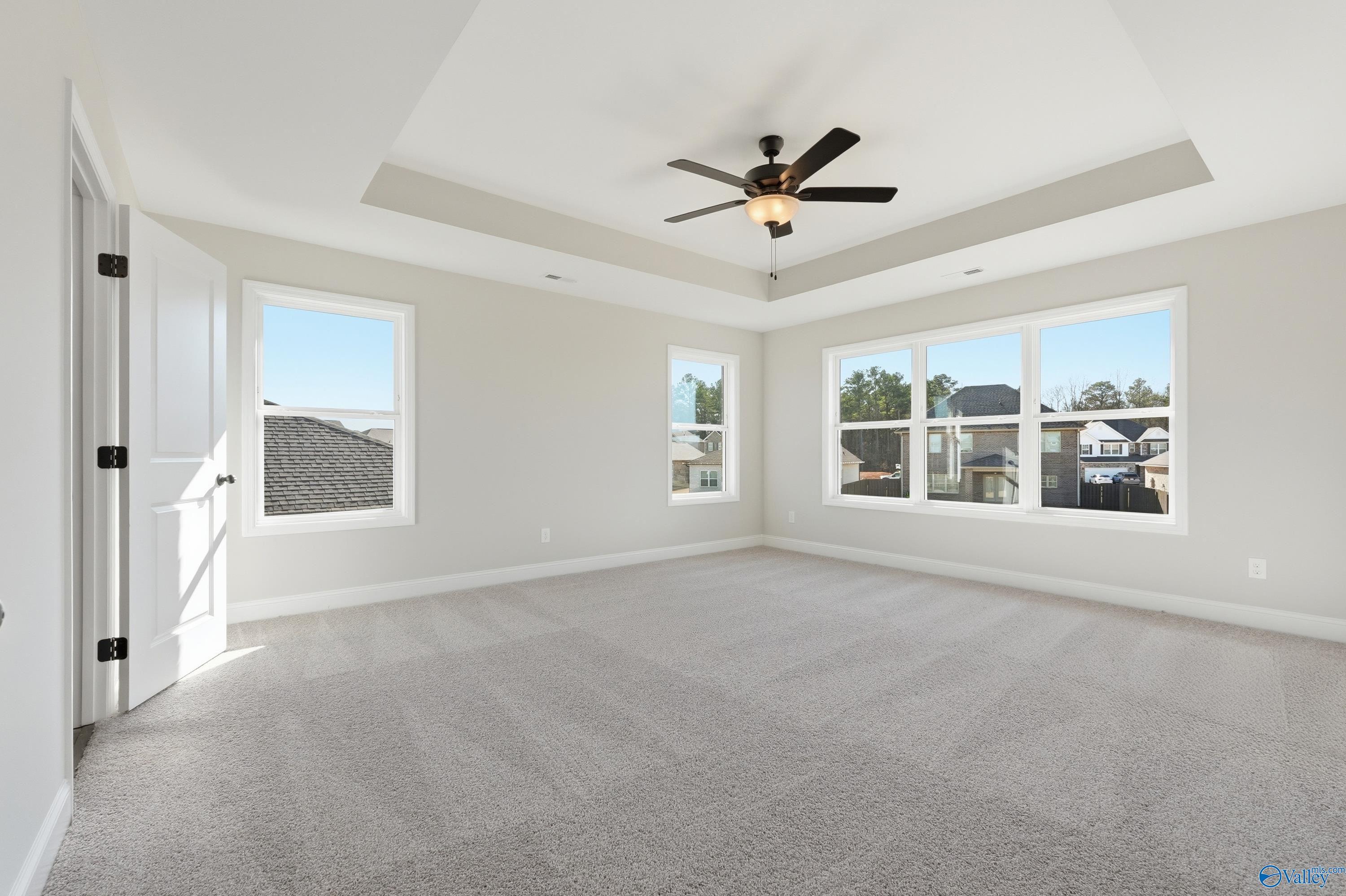 Spacious bedroom with large windows, tray ceiling fan, beige walls, and carpet in Davidson Homes The Chelsea C, Harvest, Alabama