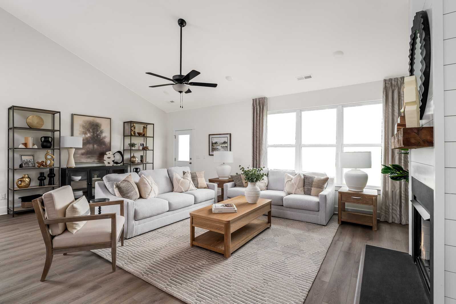 Cozy open-concept living room at Woods Crossing in Gallatin TN with beige sofas, fireplace, ceiling fan, and large windows