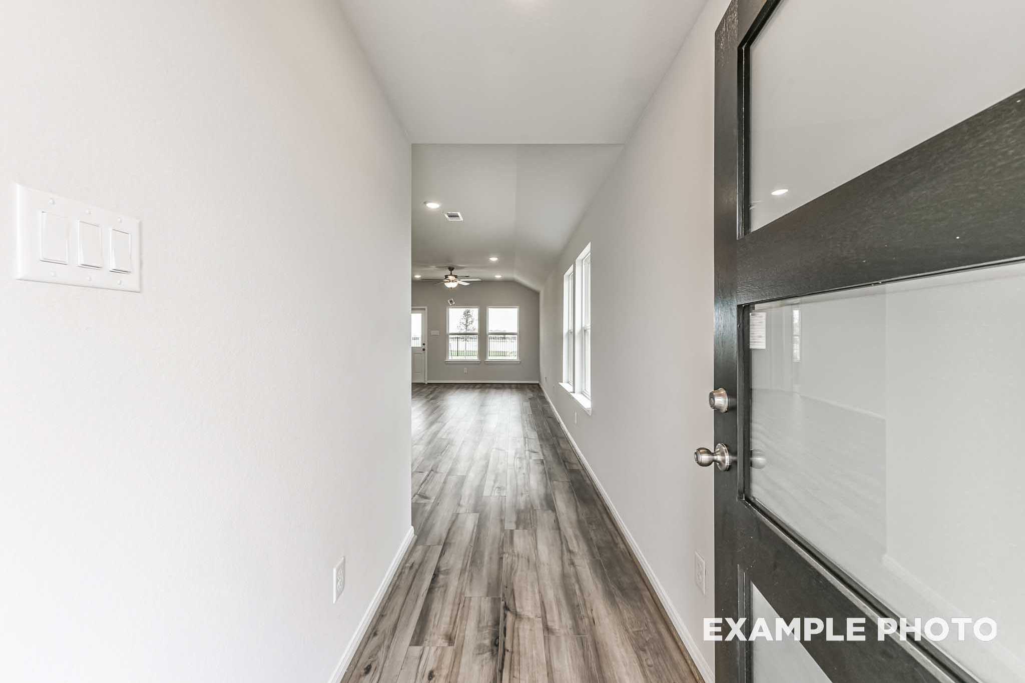 Spacious hallway in The Costa C home with light walls, hardwood floors, and modern black glass-paneled door