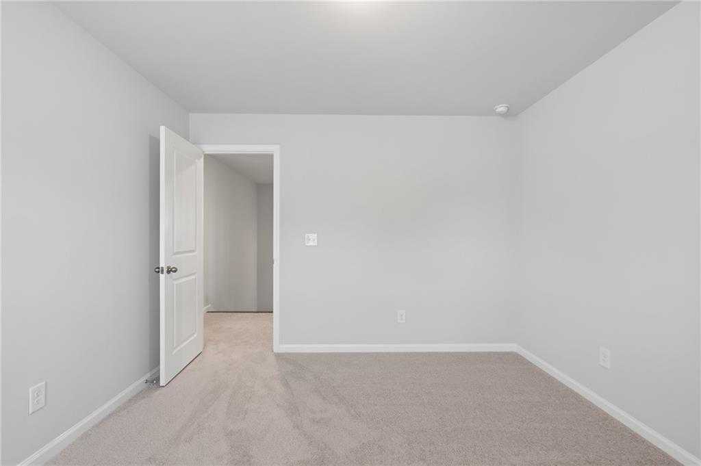 Empty secondary bedroom with neutral walls, beige carpet, and open hallway door in Davidson Homes The Hickory B, Winder, GA