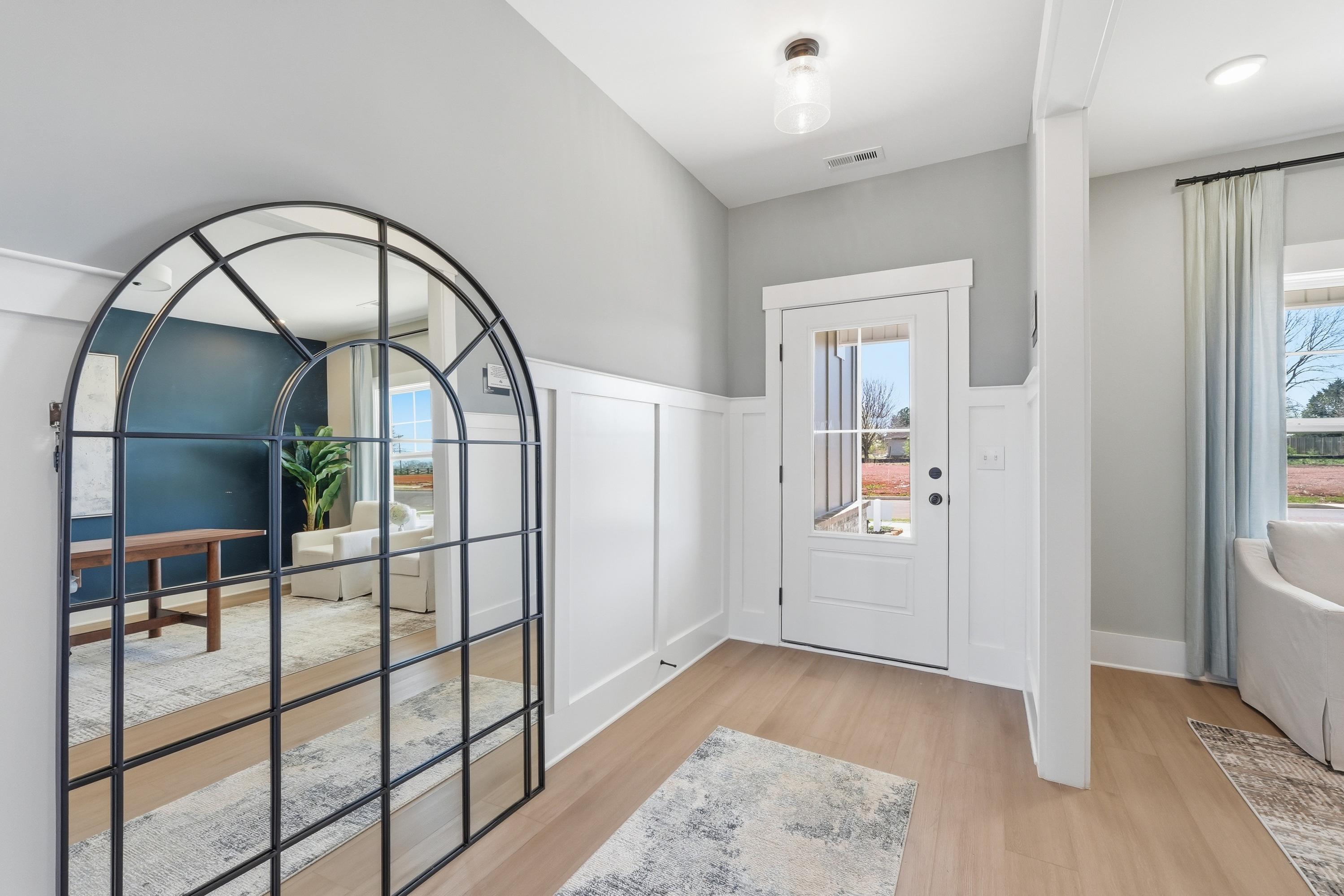 Spacious entryway at Berry Cove in New Market Alabama featuring arched black mirror, light hardwood floors, and white paneled door