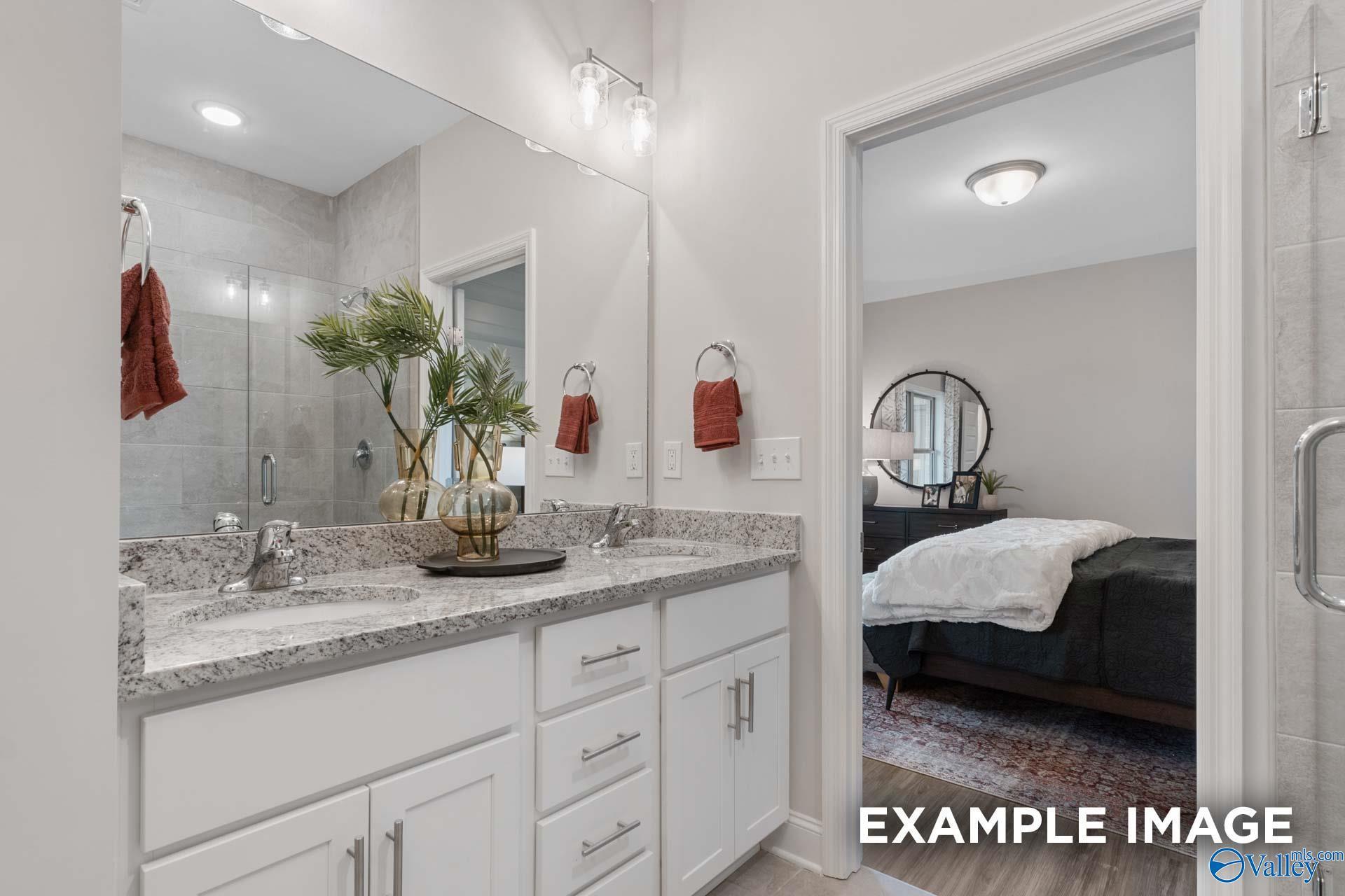 Double vanity bathroom with granite countertops and tile shower adjoining primary bedroom in Davidson Homes Camilla C, Hartselle