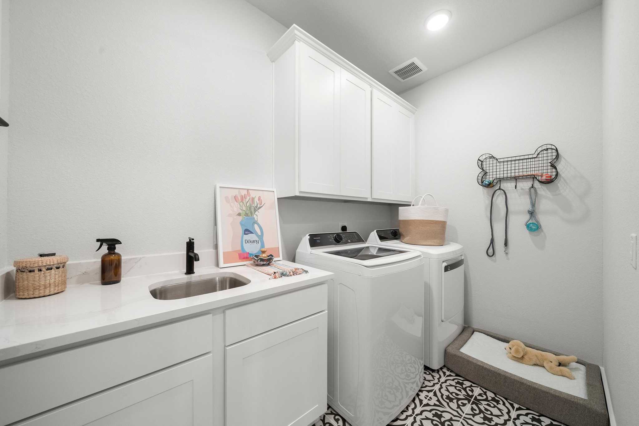 Modern laundry room in Lago Mar Texas City TX with white cabinets washer dryer utility sink and pet bed by Davidson Homes