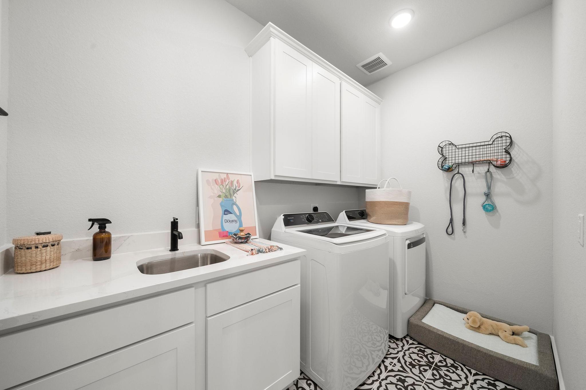 Modern laundry room in Lago Mar Texas City TX with white cabinets washer dryer utility sink and pet bed by Davidson Homes