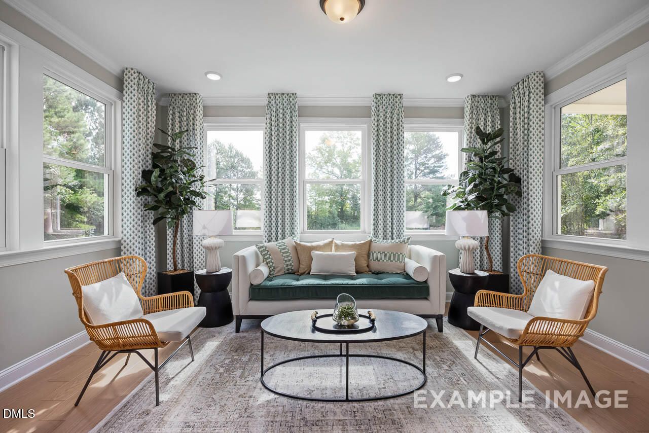 Bright sunroom with large windows, green velvet sofa, wicker chairs, potted plants in Davidson Homes The Crawford D, Angier, NC