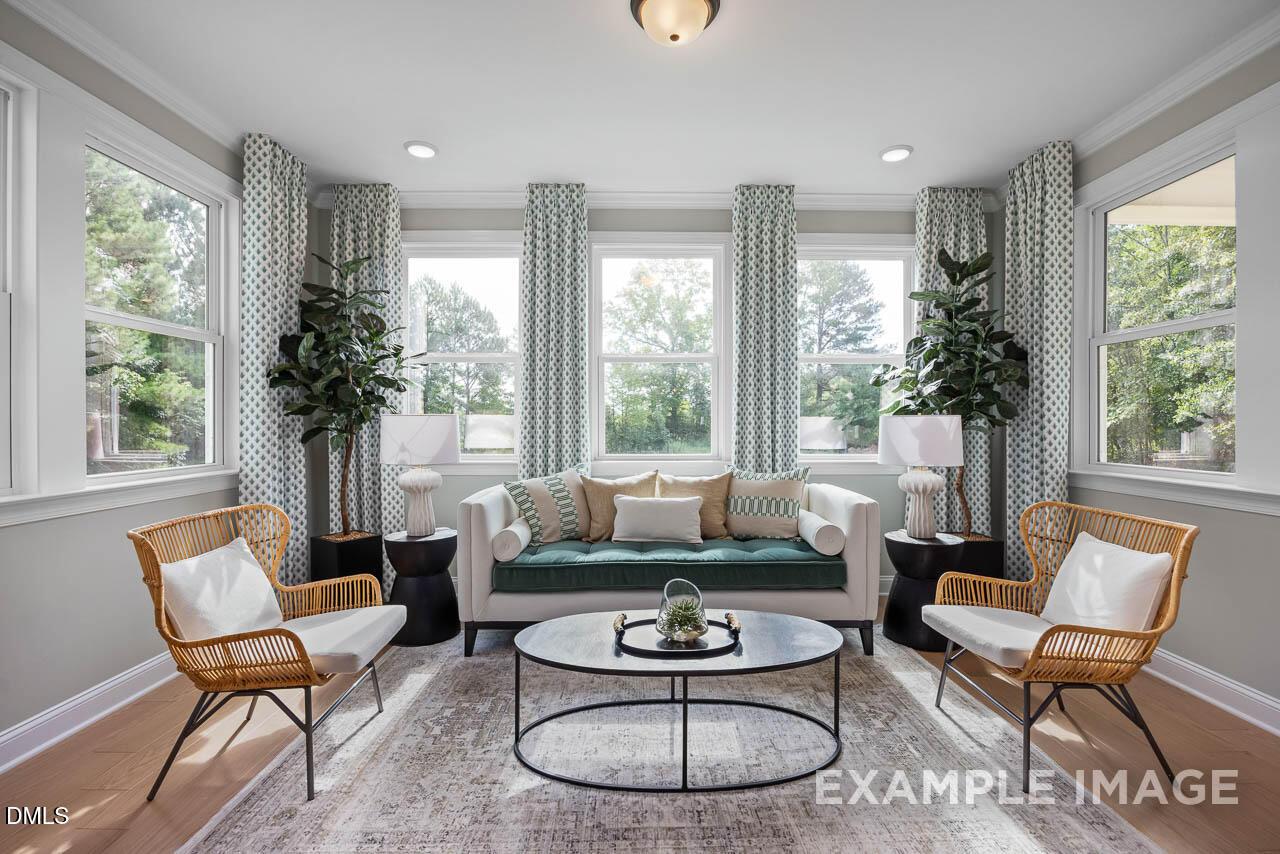 Bright sunroom with large windows, green velvet sofa, wicker chairs, potted plants in Davidson Homes The Crawford D, Angier, NC