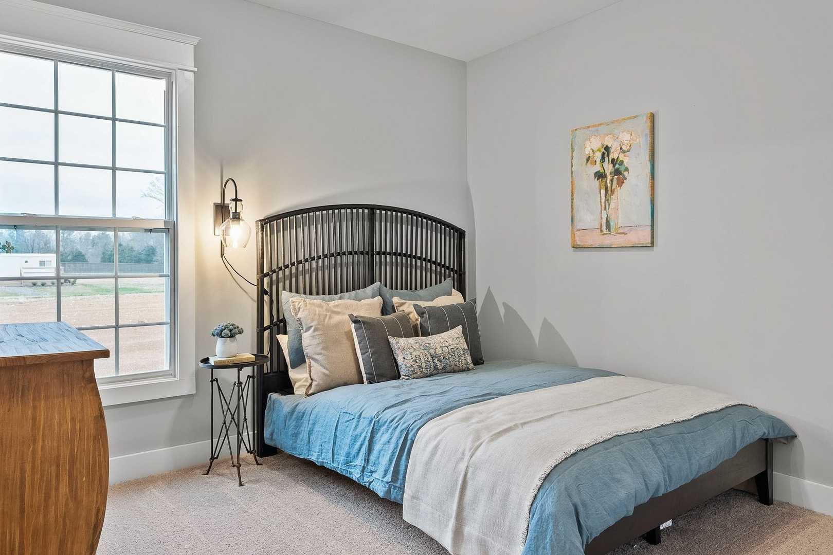 Cozy bedroom in The Oxford with blue bedding, wrought iron headboard, gray walls, and rural window view